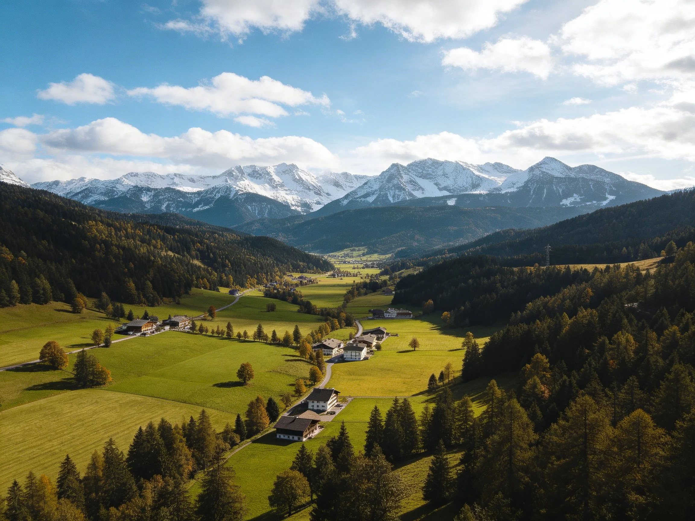 Lush valley with green fields, scattered homes, and snow-capped mountains