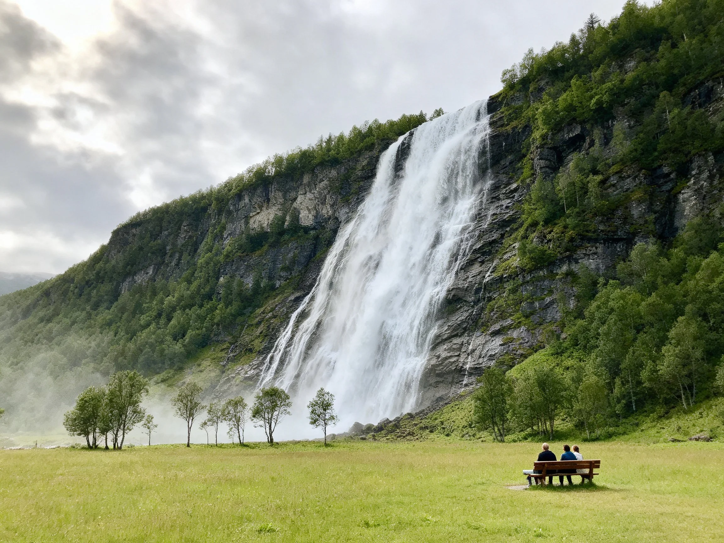 Majestic waterfall cascades down rocky cliffs beside lush green meadow