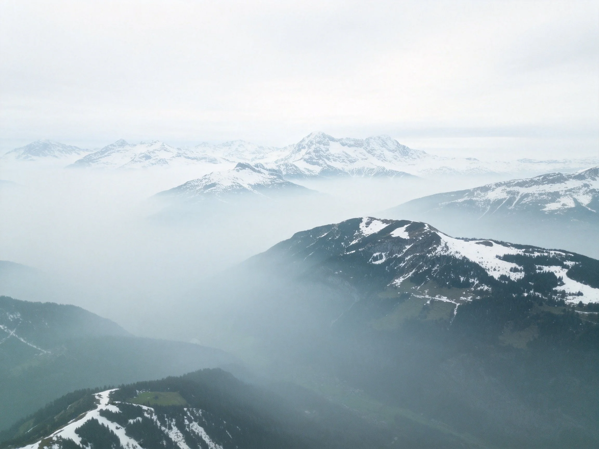 Misty Snow-Capped Peaks Over Forested Mountain Valleys