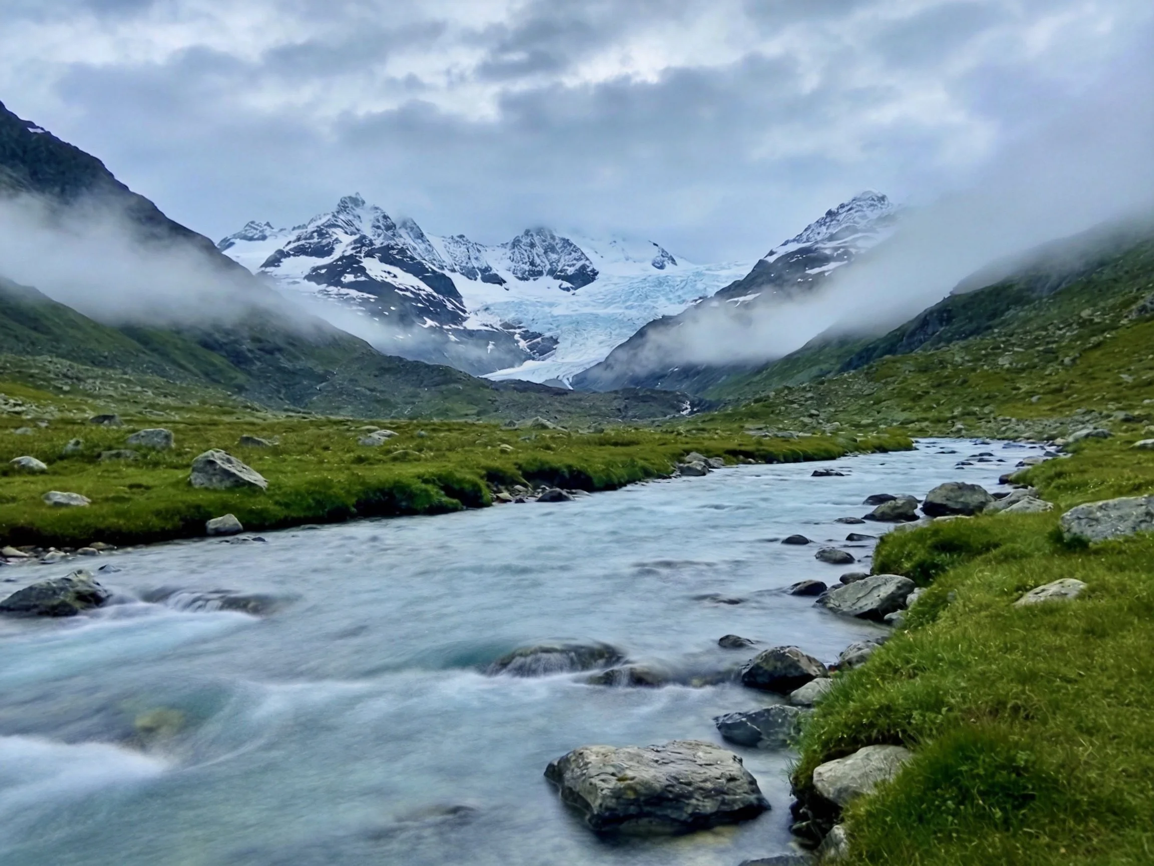 Misty valley with rushing stream near snow-capped mountains