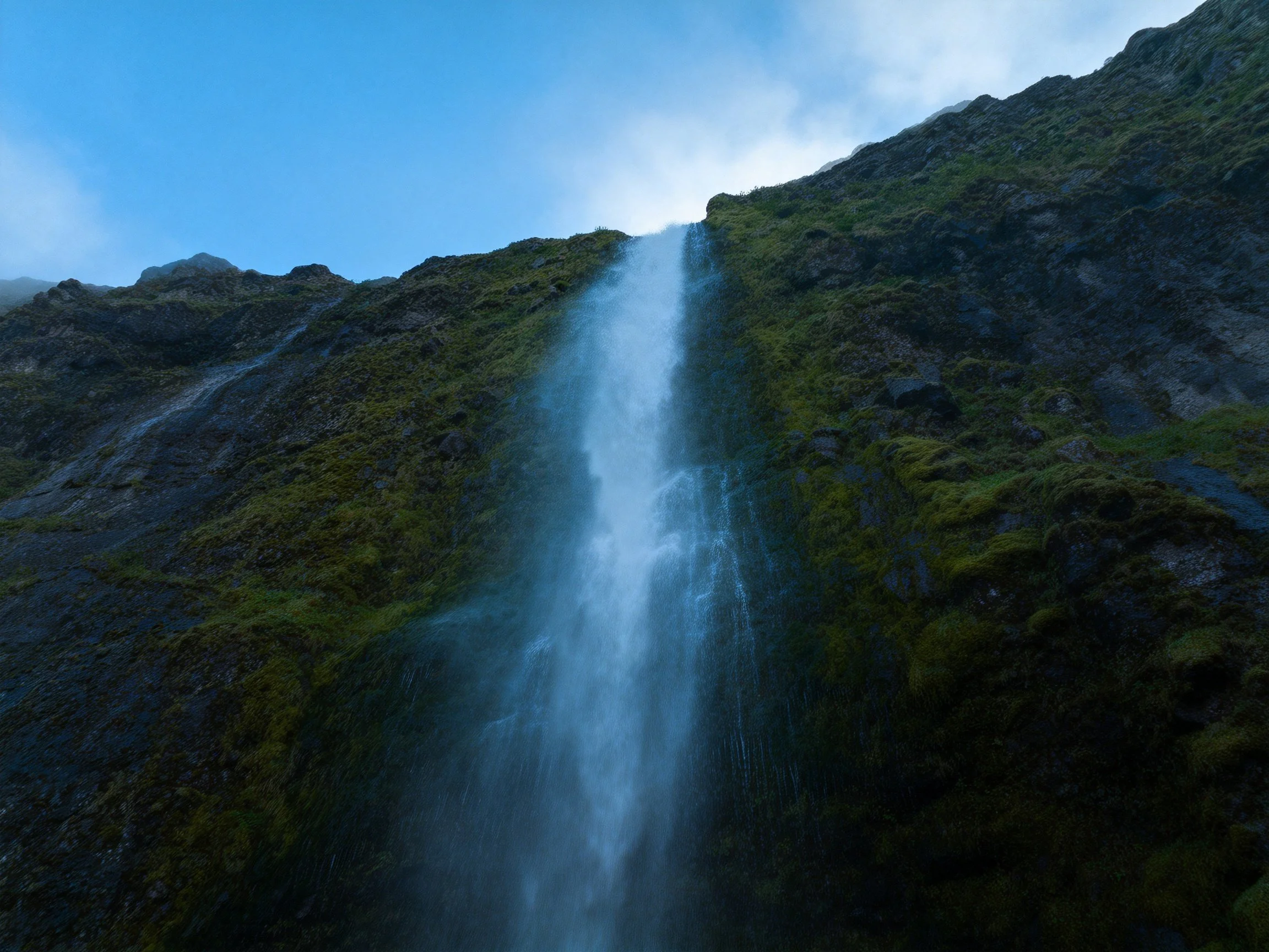 Misty waterfall cascades down mossy mountain cliffside