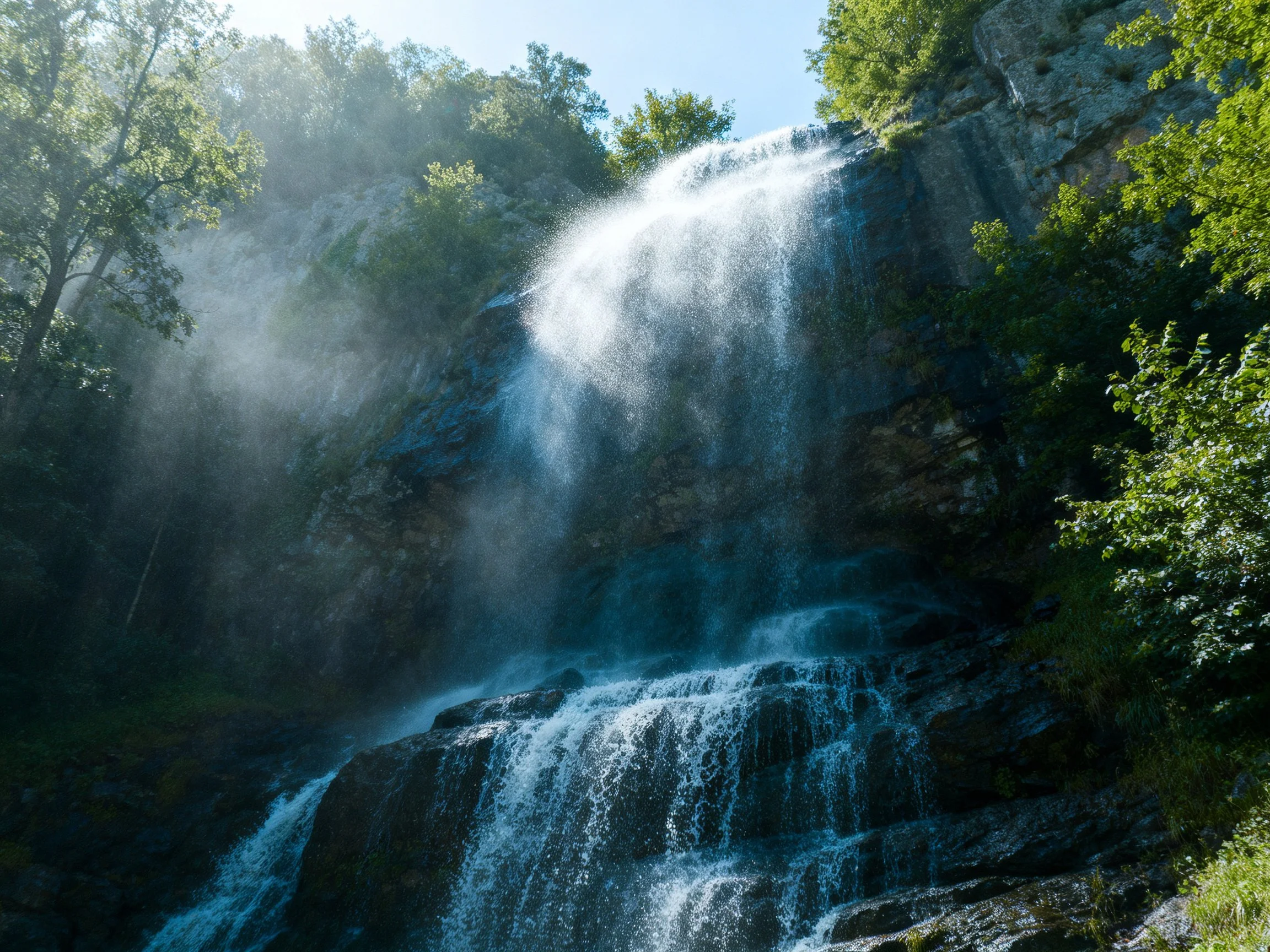 Misty waterfall cascades over dark rocky cliffs amid lush green trees