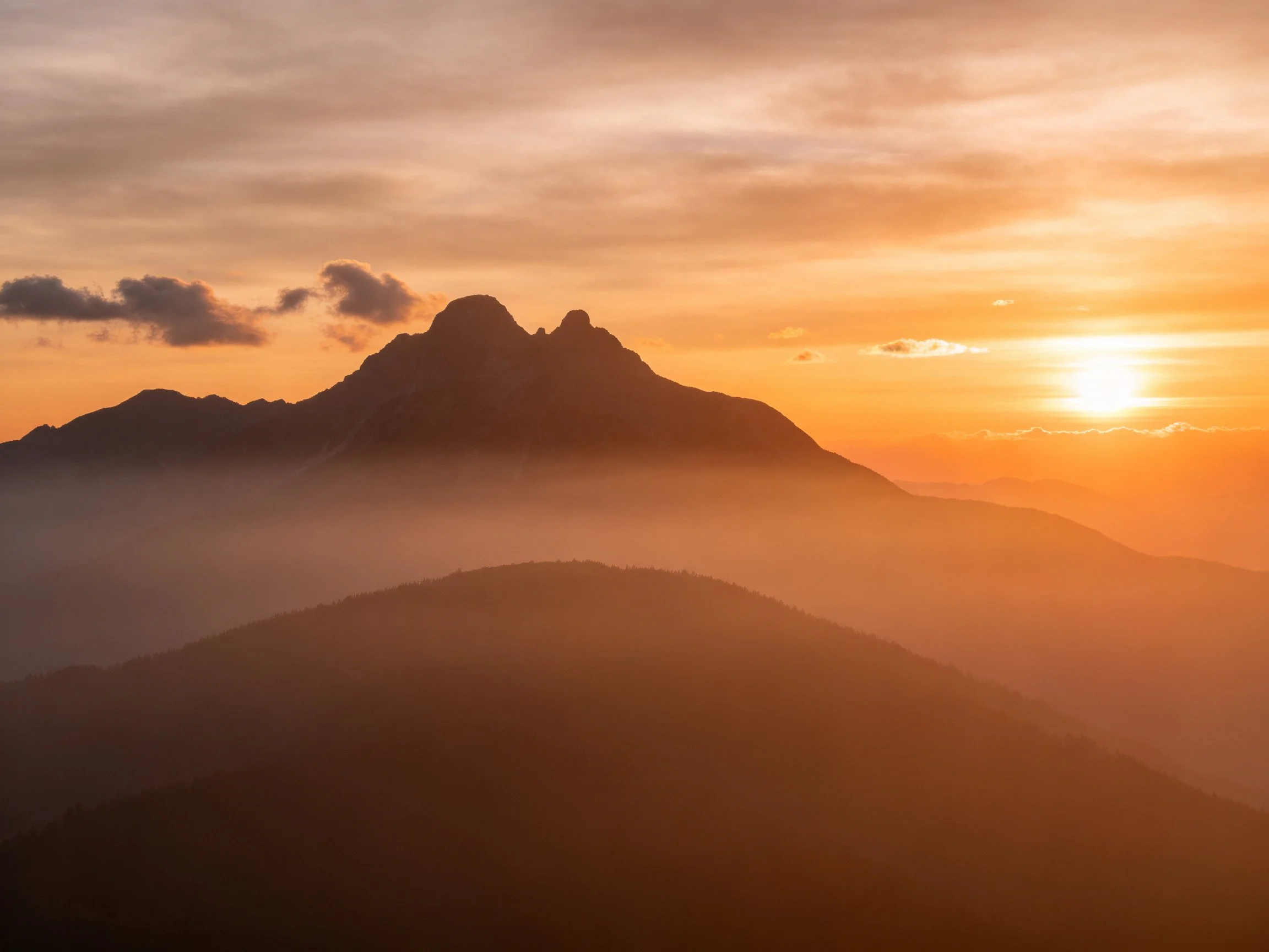 Mountain Peaks Silhouetted by Vibrant Sunset with Misty Layers