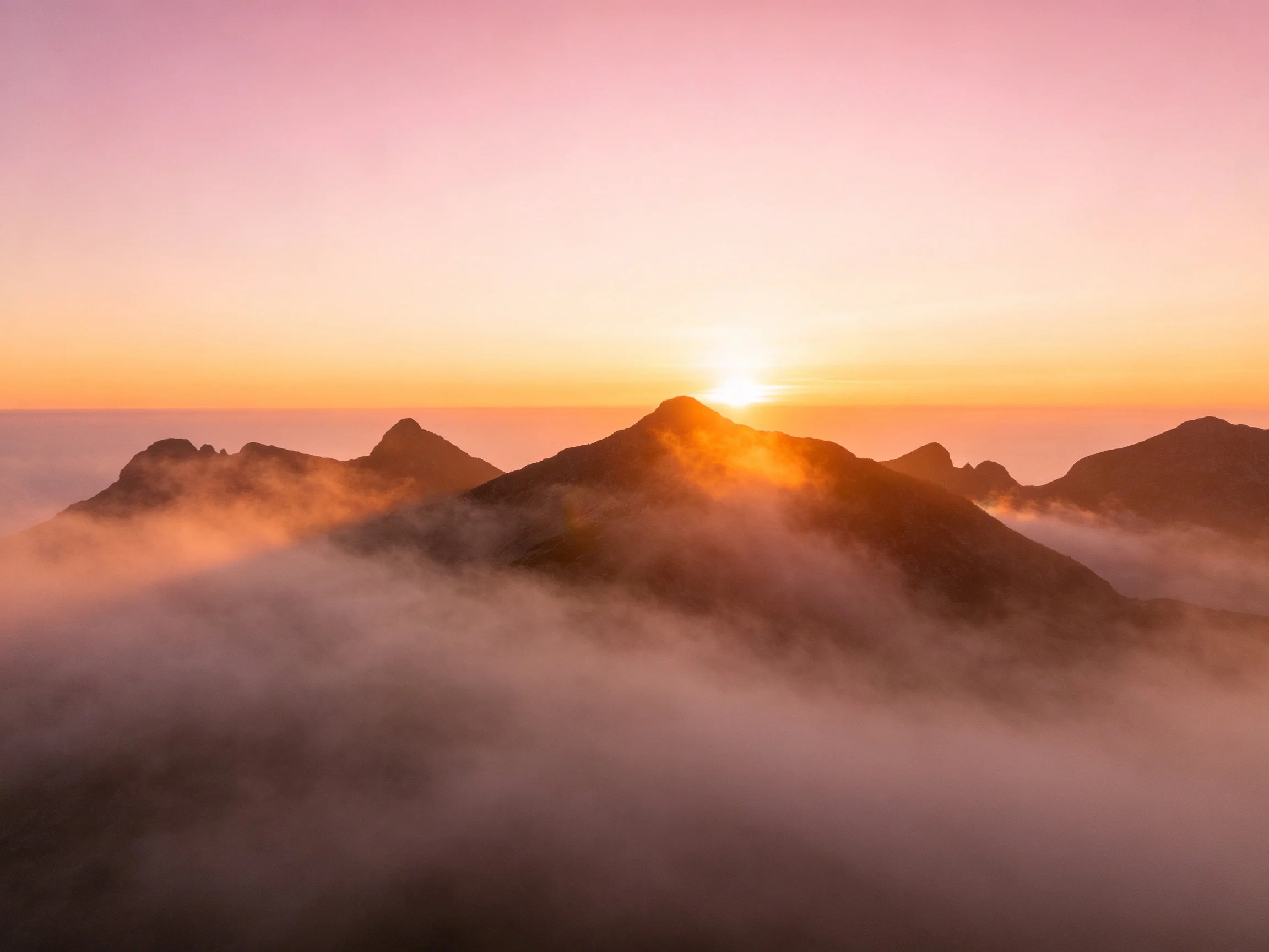 Mountain peaks rise above morning mist with golden sunrise light