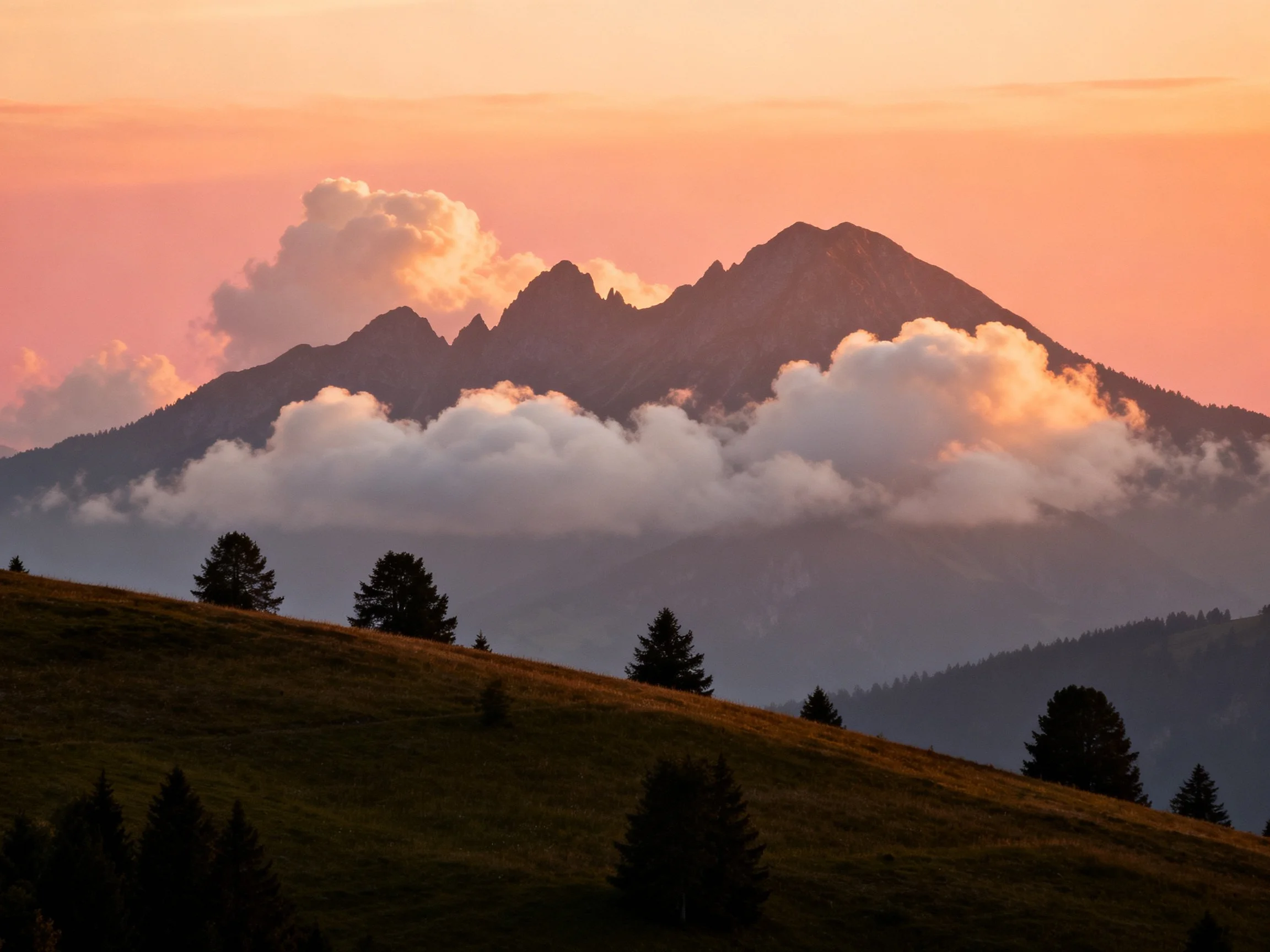 Mountain peaks shrouded in clouds at sunset with forested foreground