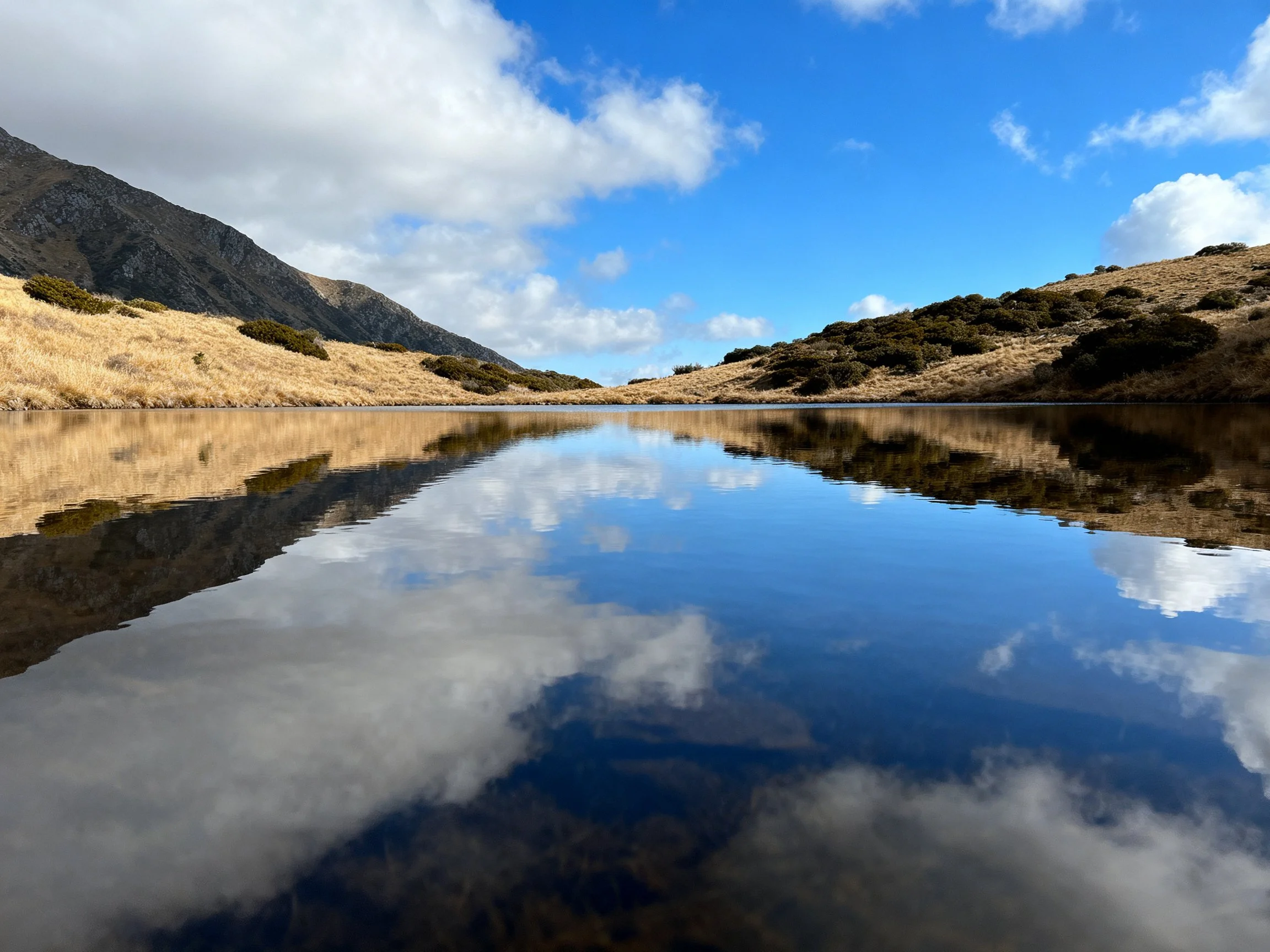 Mountainous terrain reflected in glassy water under bright sky
