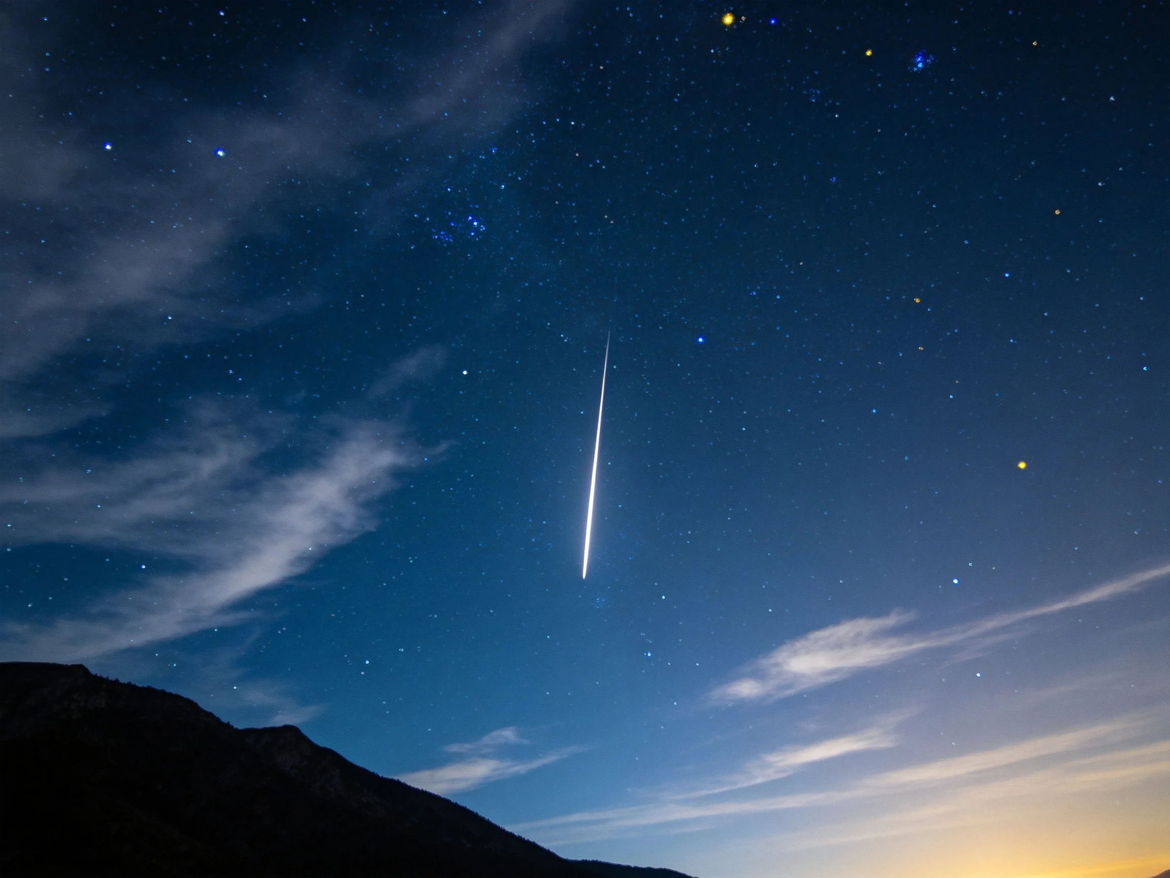 Night sky with a shooting star, scattered stars, and mountain silhouette