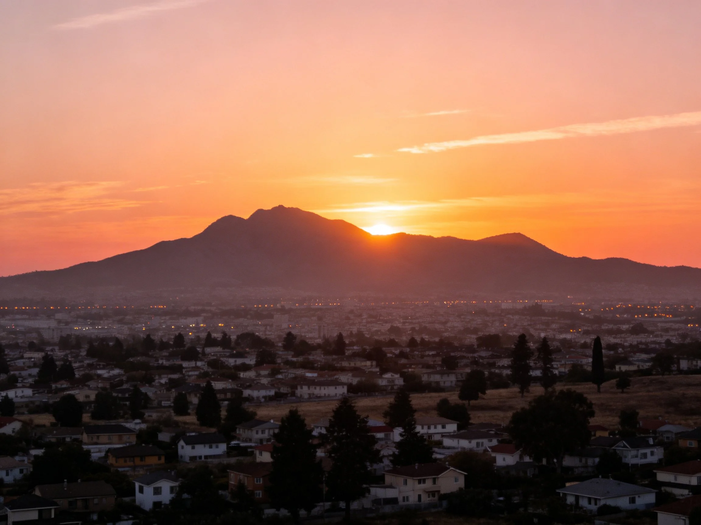 Orange sunset behind mountain silhouette, suburban town below