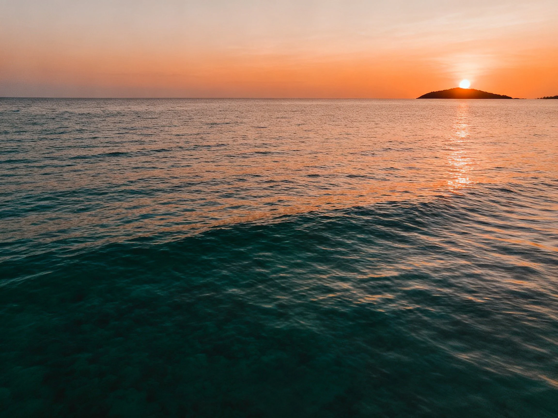 Orange sunset over turquoise ocean near dark island