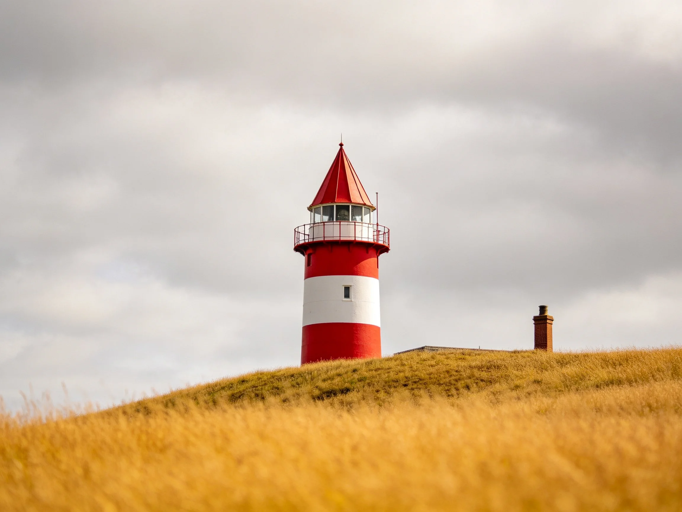 Red and white striped lighthouse atop golden grassy hill under cloudy sky