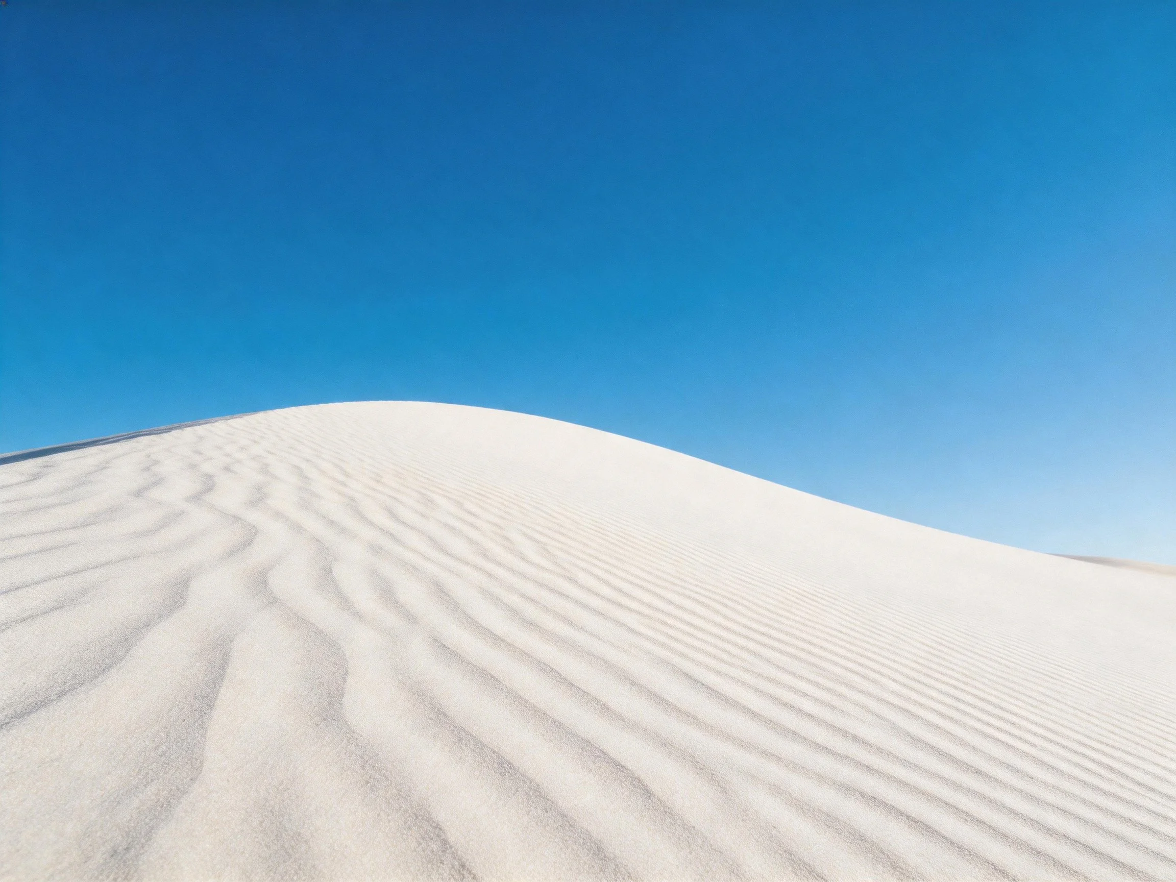 Rippled white sand dunes under clear blue sky