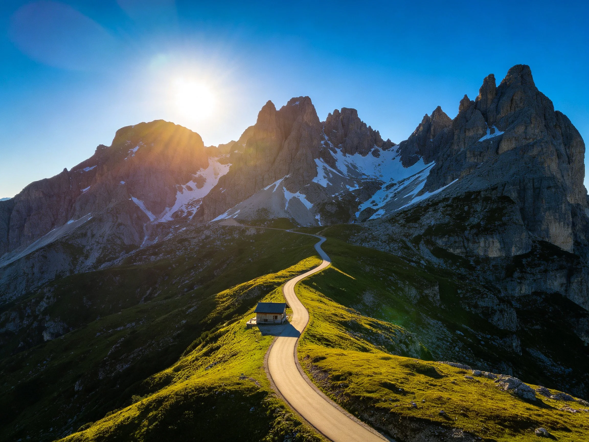 Rocky mountain peaks with winding road, bright sun, and lush green hills