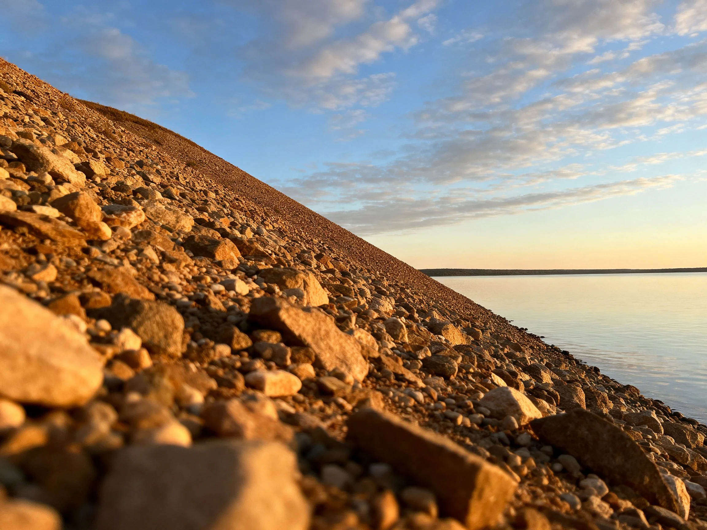 Rocky slope near calm water under a partly cloudy sky