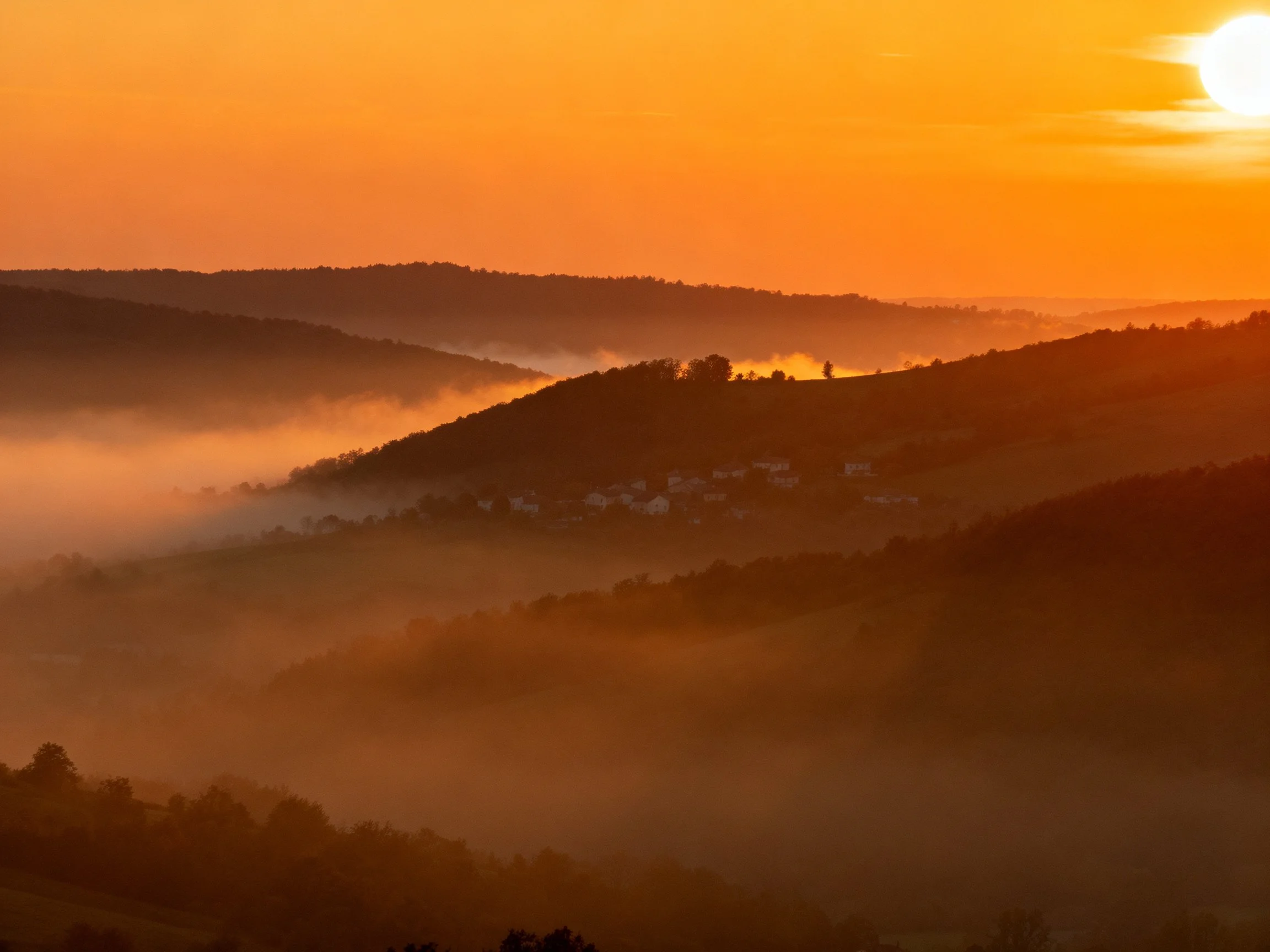 Rolling hills bathed in vibrant orange sunset with morning mist