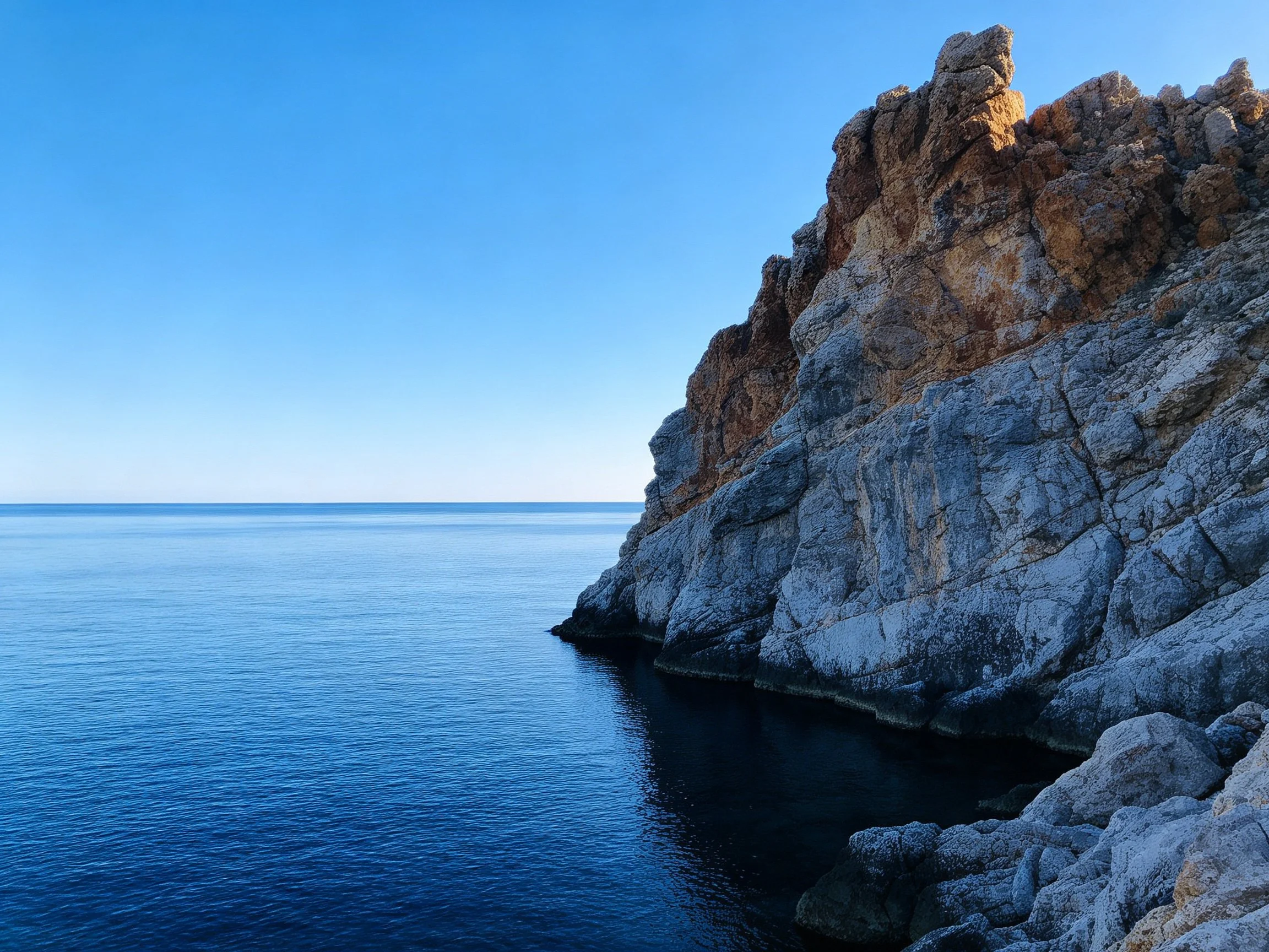 Rugged cliffs meet serene deep-blue waters beneath clear sky