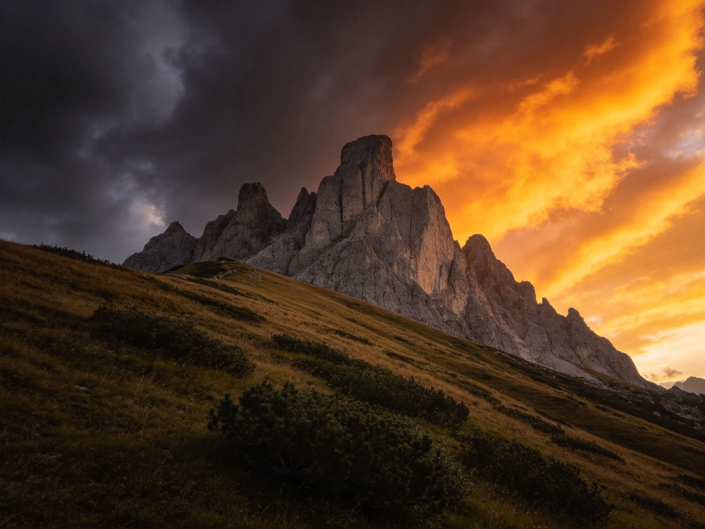 Rugged mountain peaks beneath a sky split between dark storm clouds and golden sunset