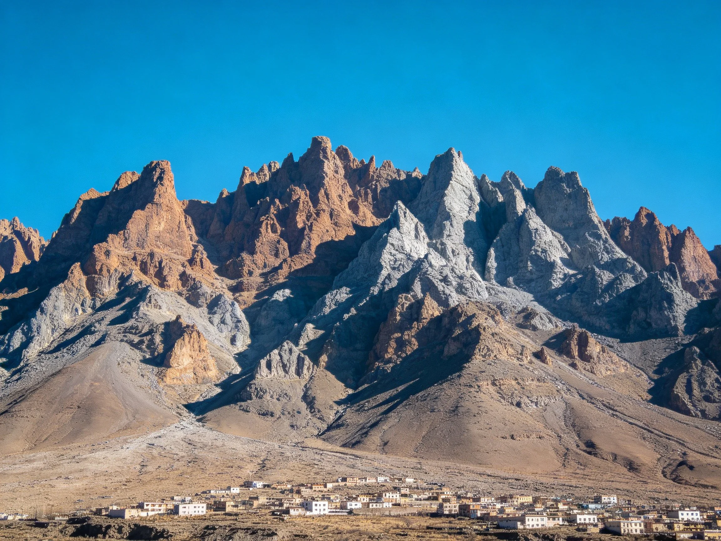 Rugged mountain range with earth-toned peaks and a small village below