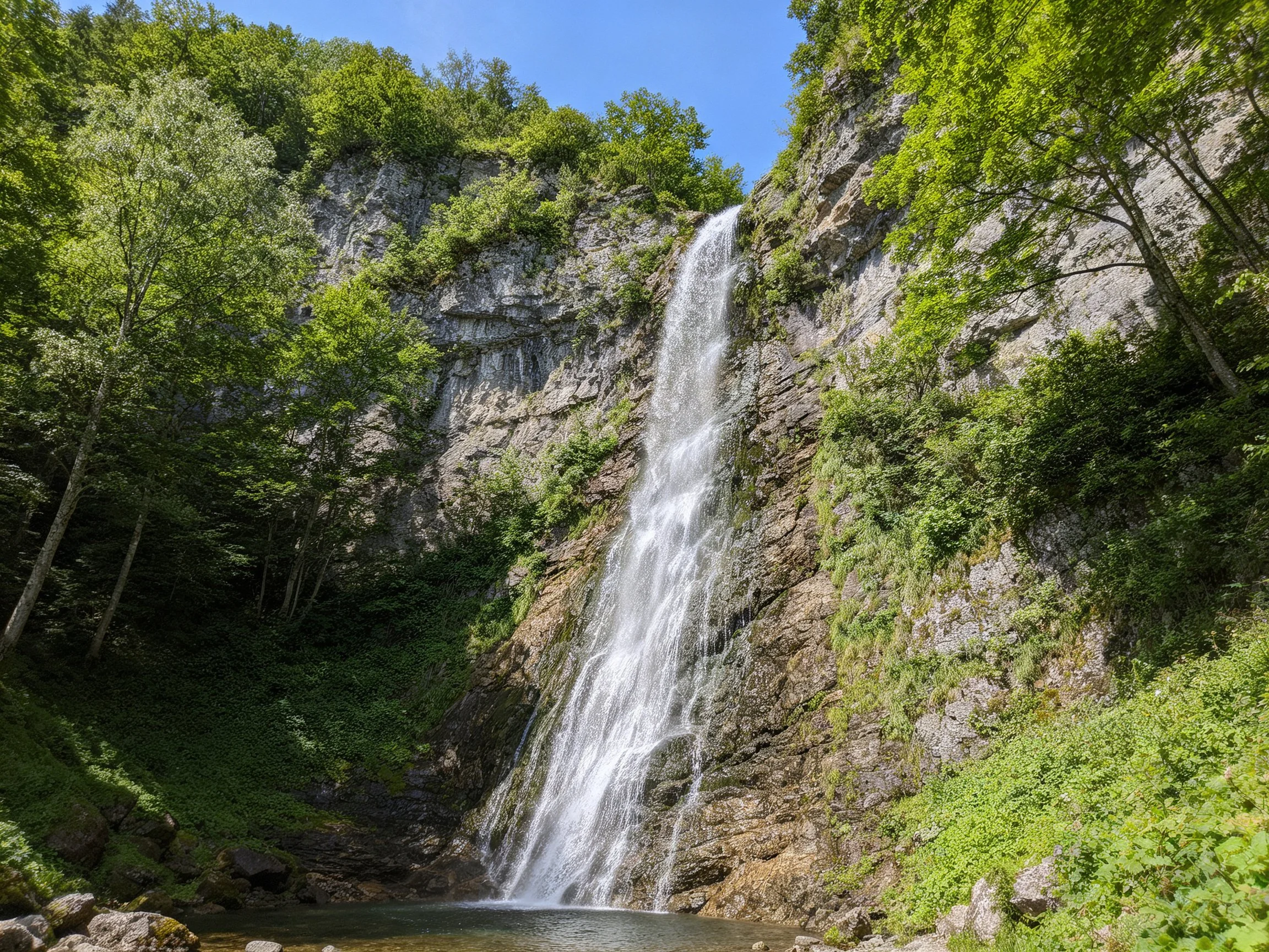 Rugged waterfall flows down steep cliff among lush green trees