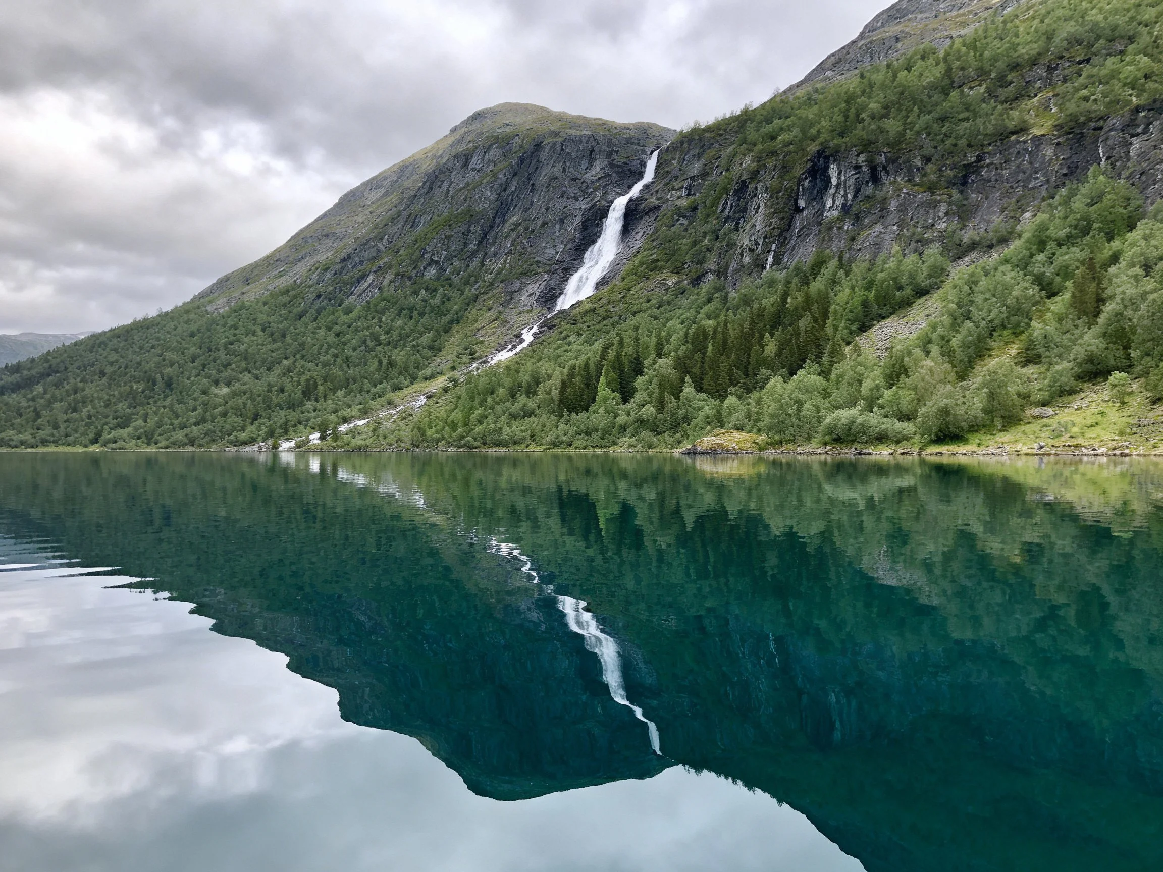 Serene mountain waterfall reflecting in turquoise lake with forested slopes