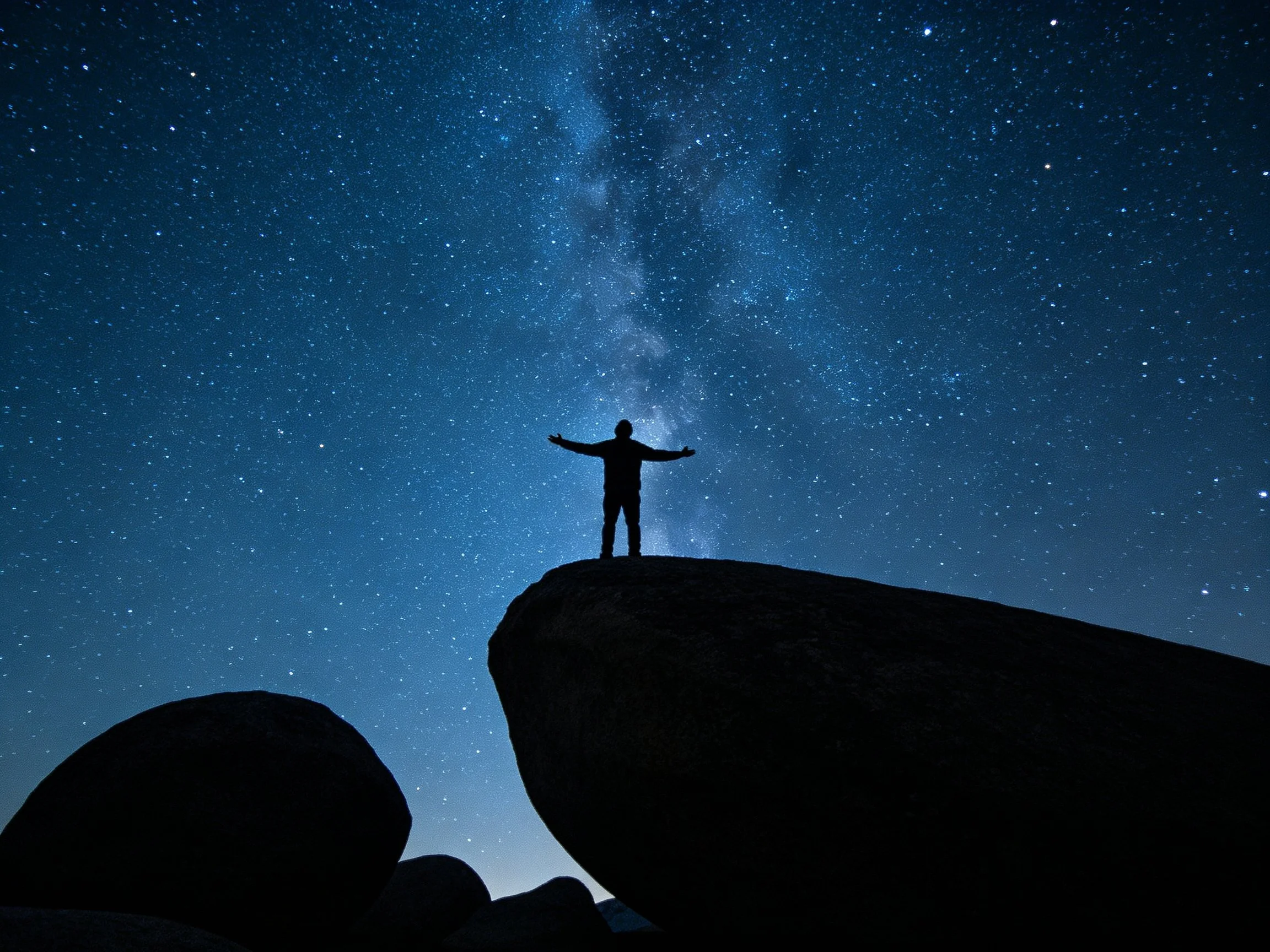 Silhouette of person on rock under star-filled night sky
