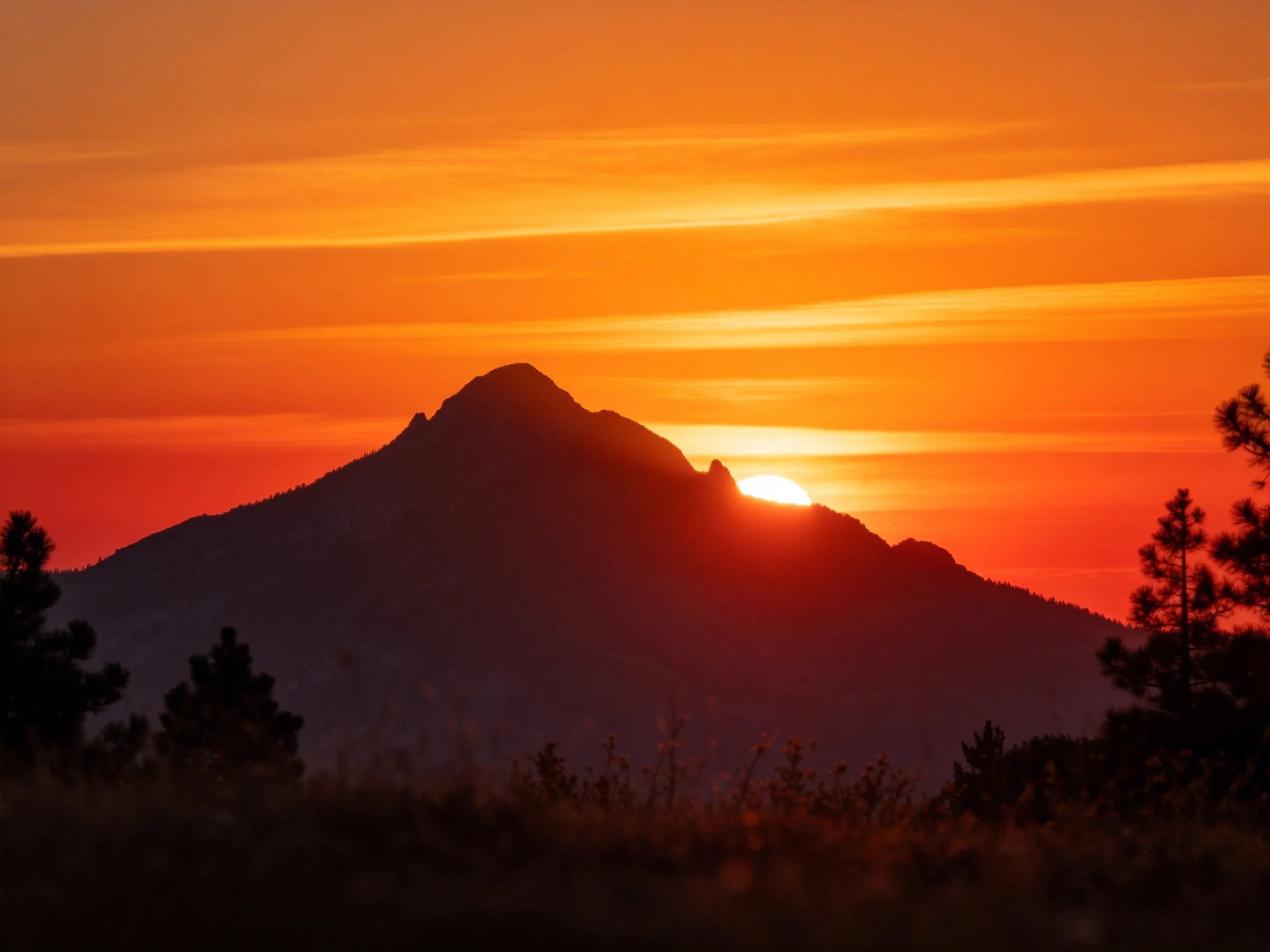 Silhouetted Mountain with Fiery Sunset and Tree Foreground