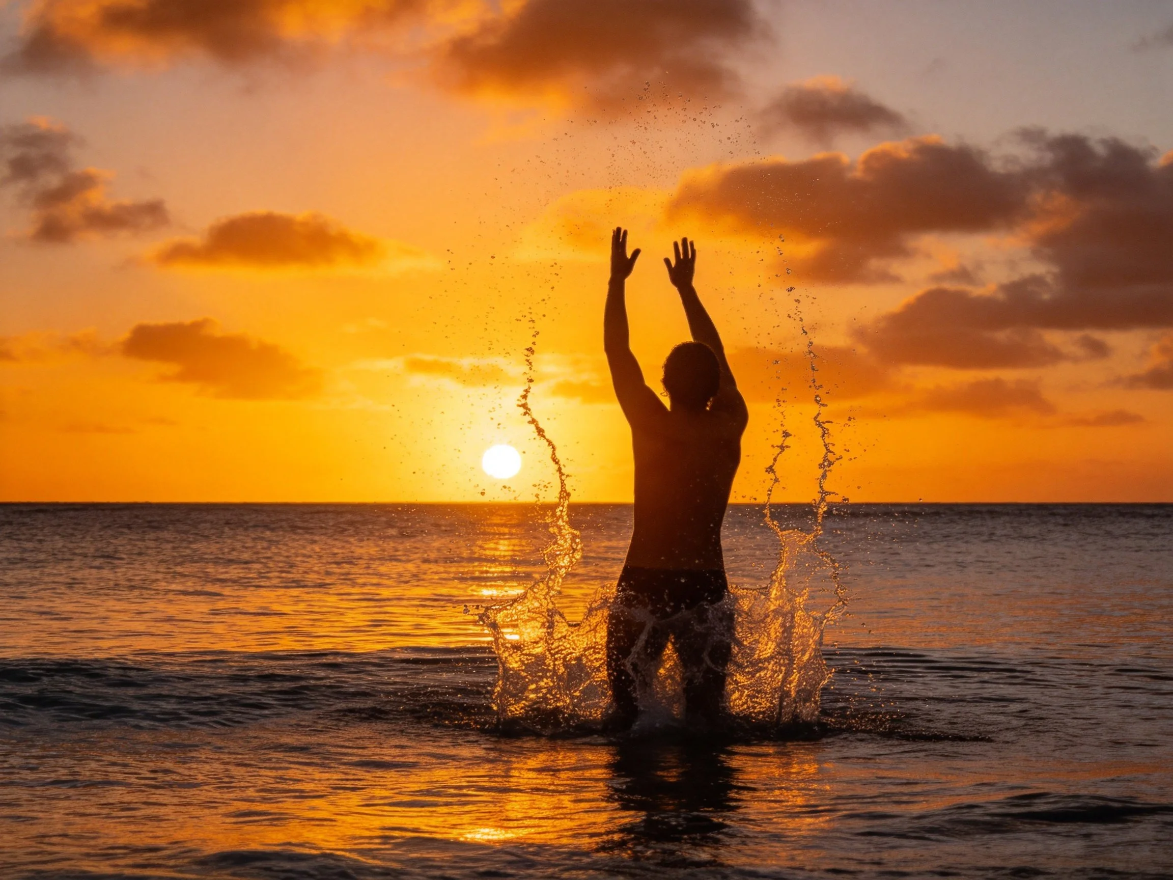 Silhouetted figure splashing in ocean during golden sunset