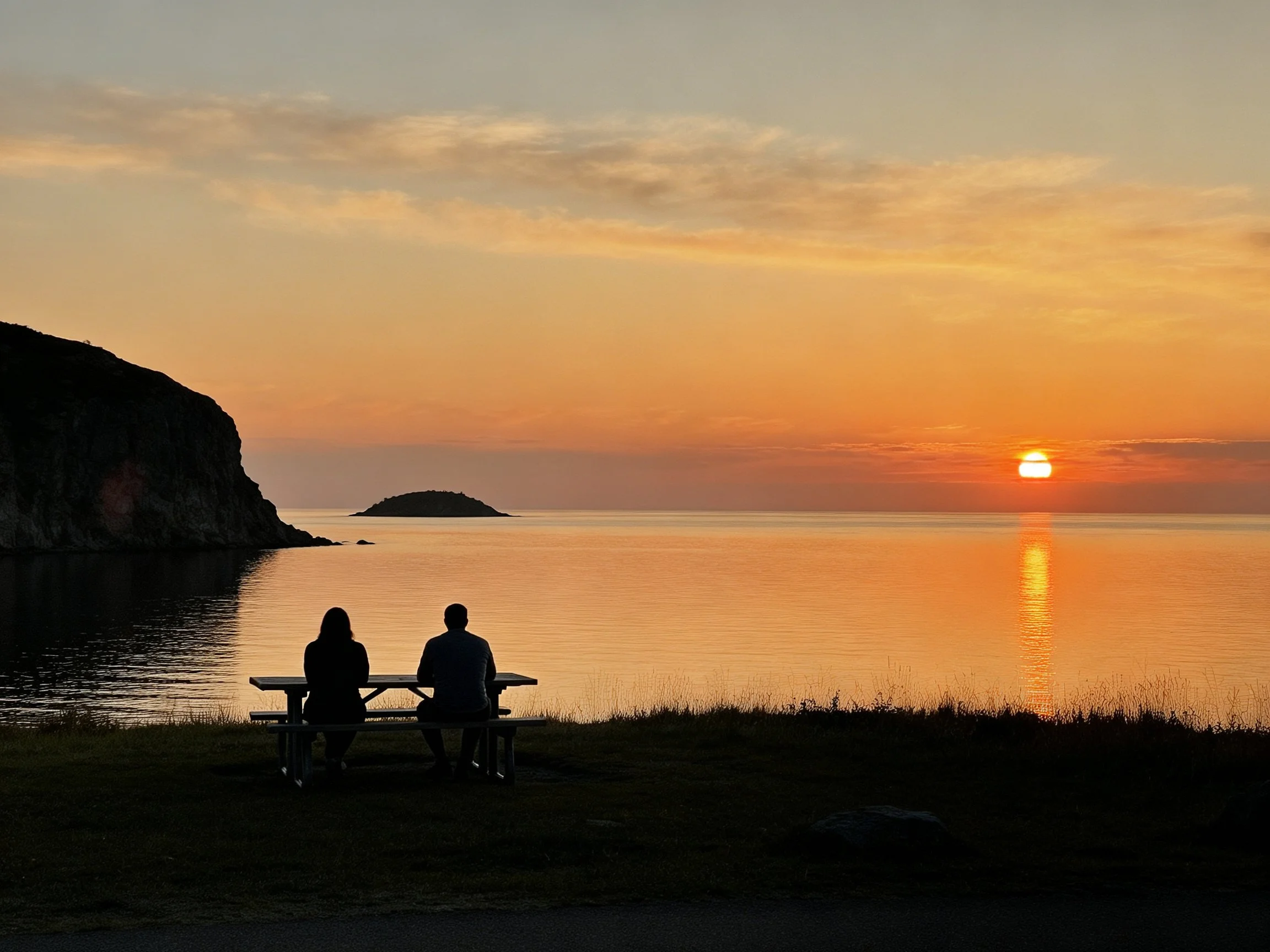Silhouetted figures at picnic table by calm ocean sunset