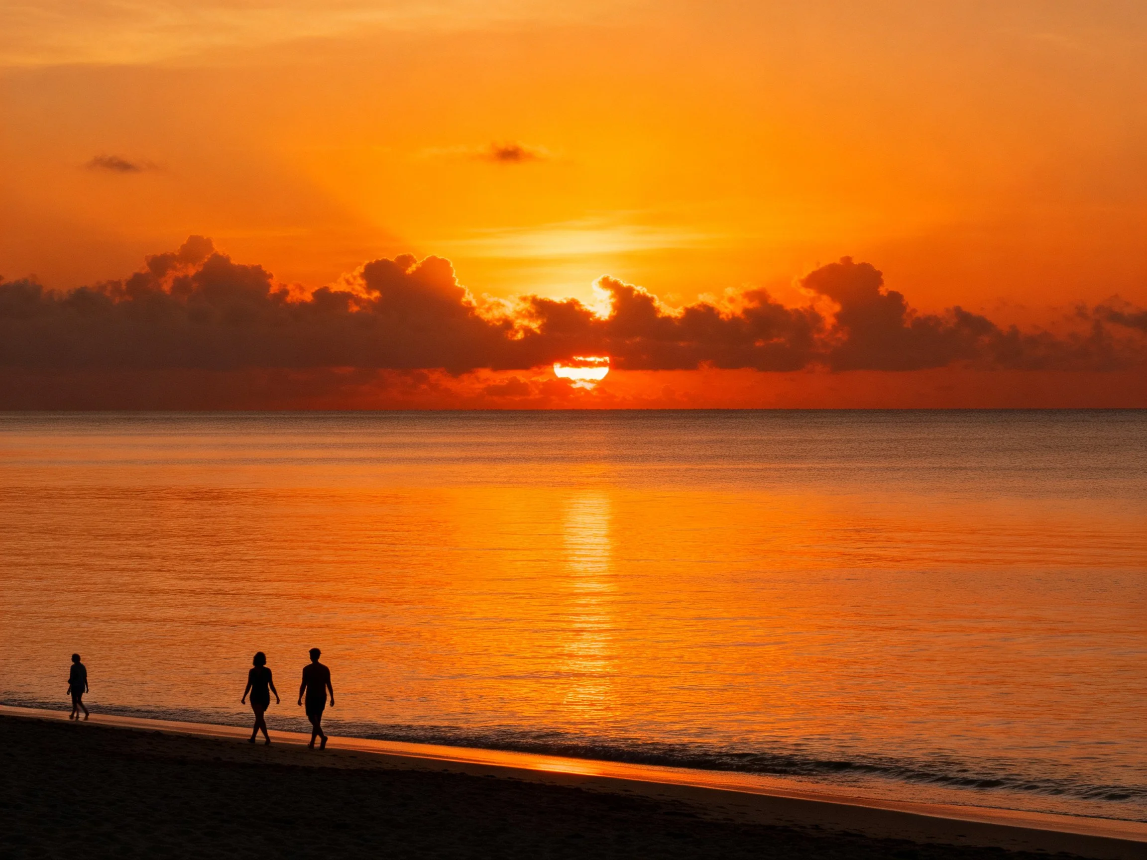 Silhouetted figures walk along a golden-orange beach at sunset