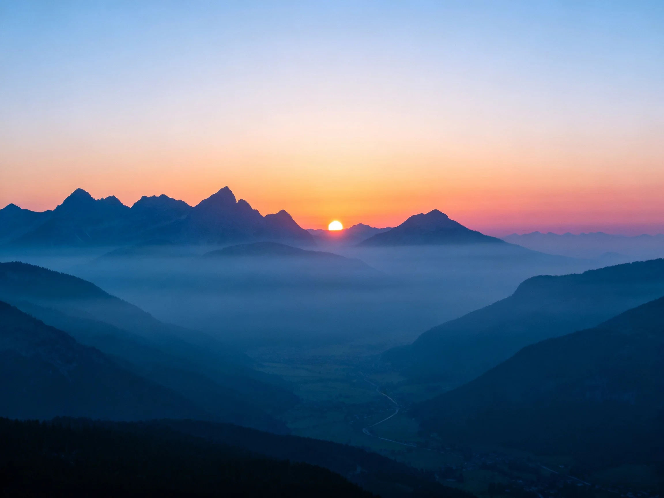 Silhouetted mountain ranges under a colorful dawn sky with misty valleys