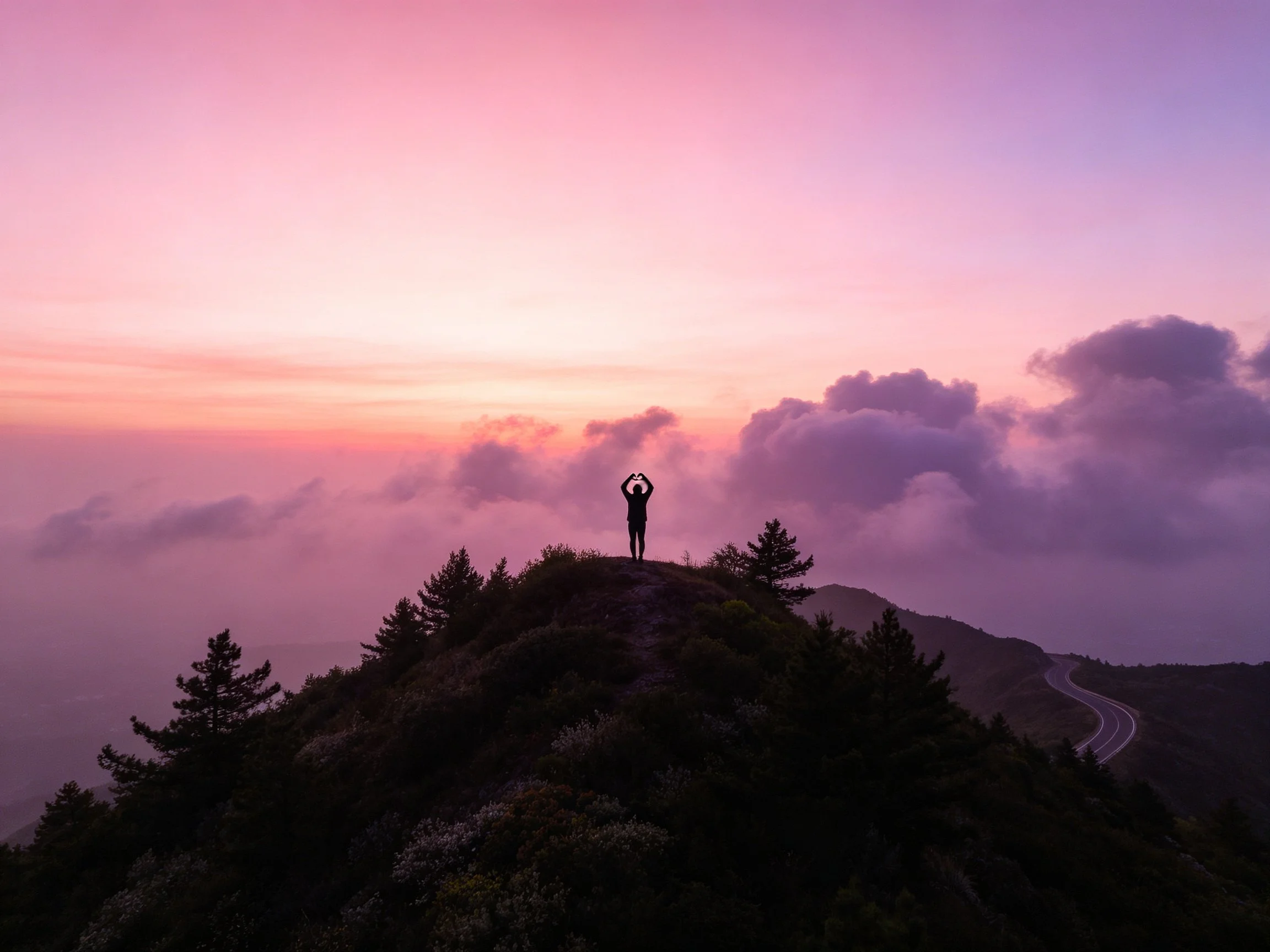 Silhouetted person on hilltop under pink-purple dusk sky with clouds