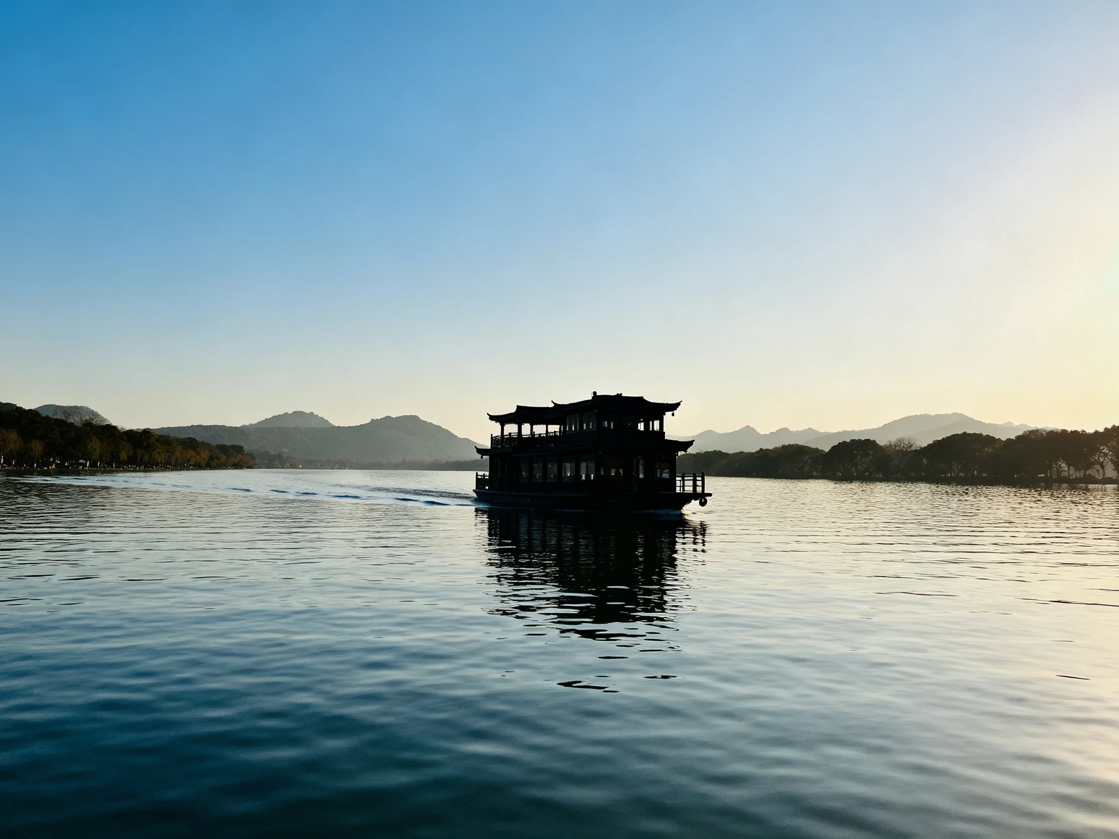 Silhouetted traditional boat on serene lake with mountainous backdrop