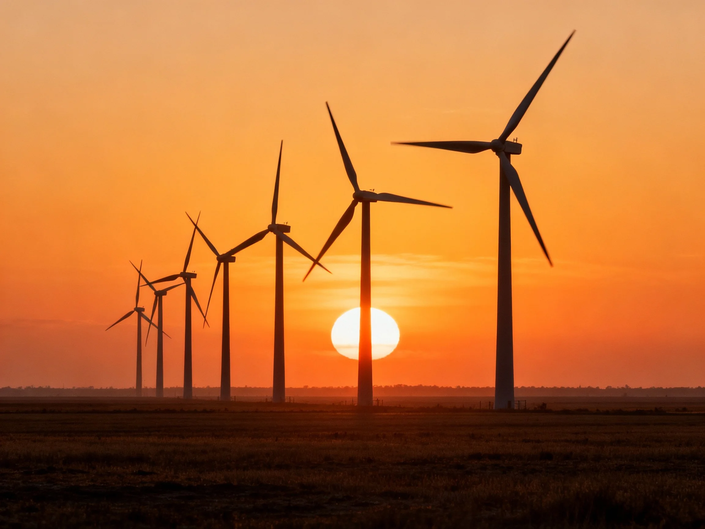 Silhouetted wind turbines aligned under a vibrant orange sunset