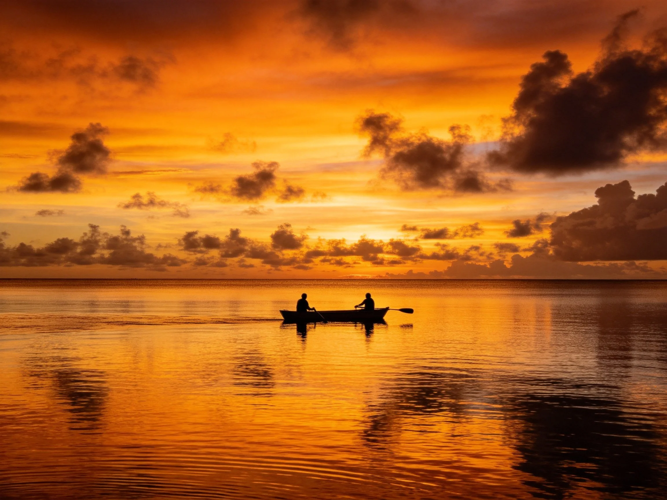 Silhouettes of two people canoeing under an orange sunset sky