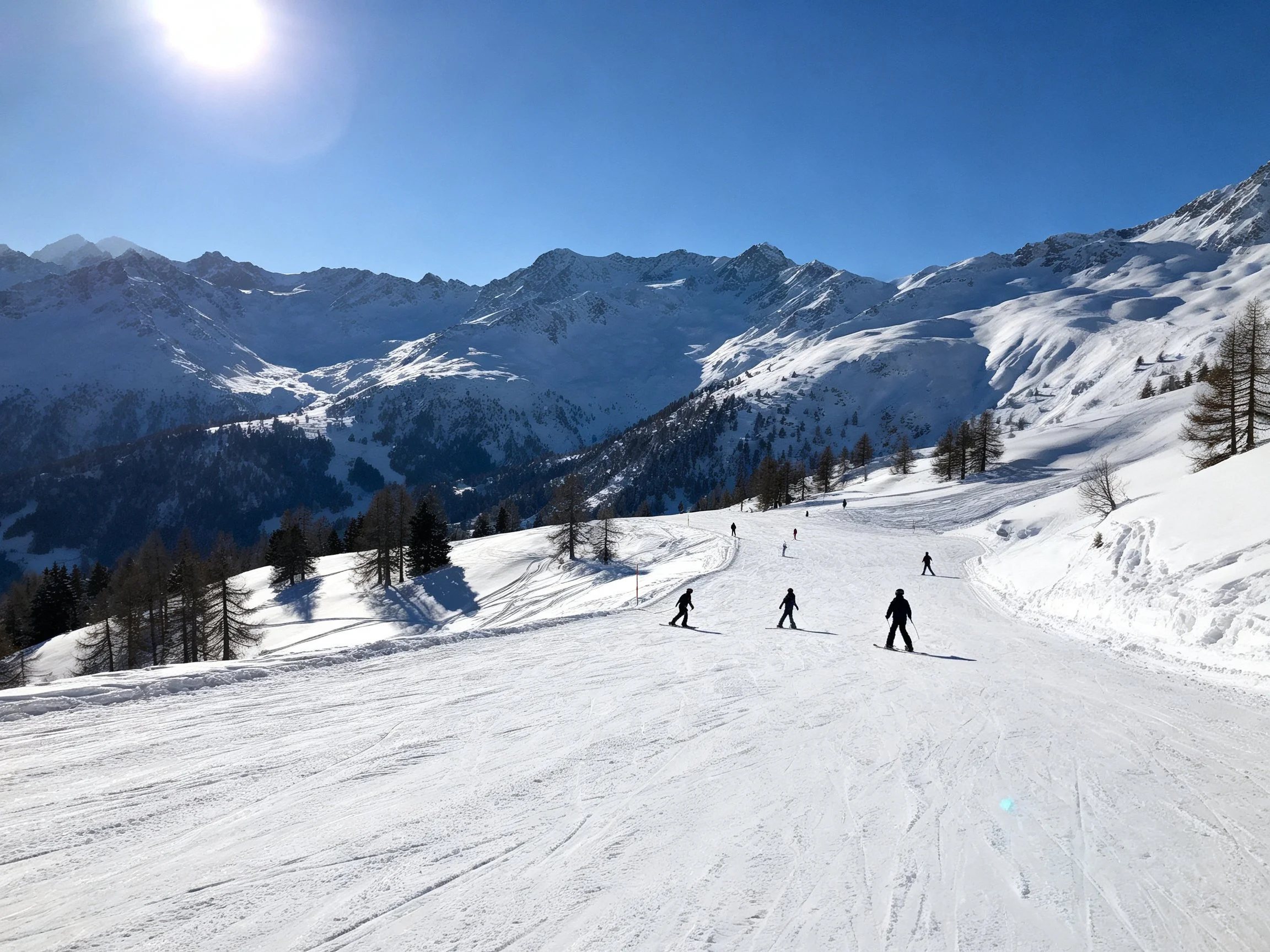 Skiers glide down a sunlit snowy mountain slope with clear blue skies
