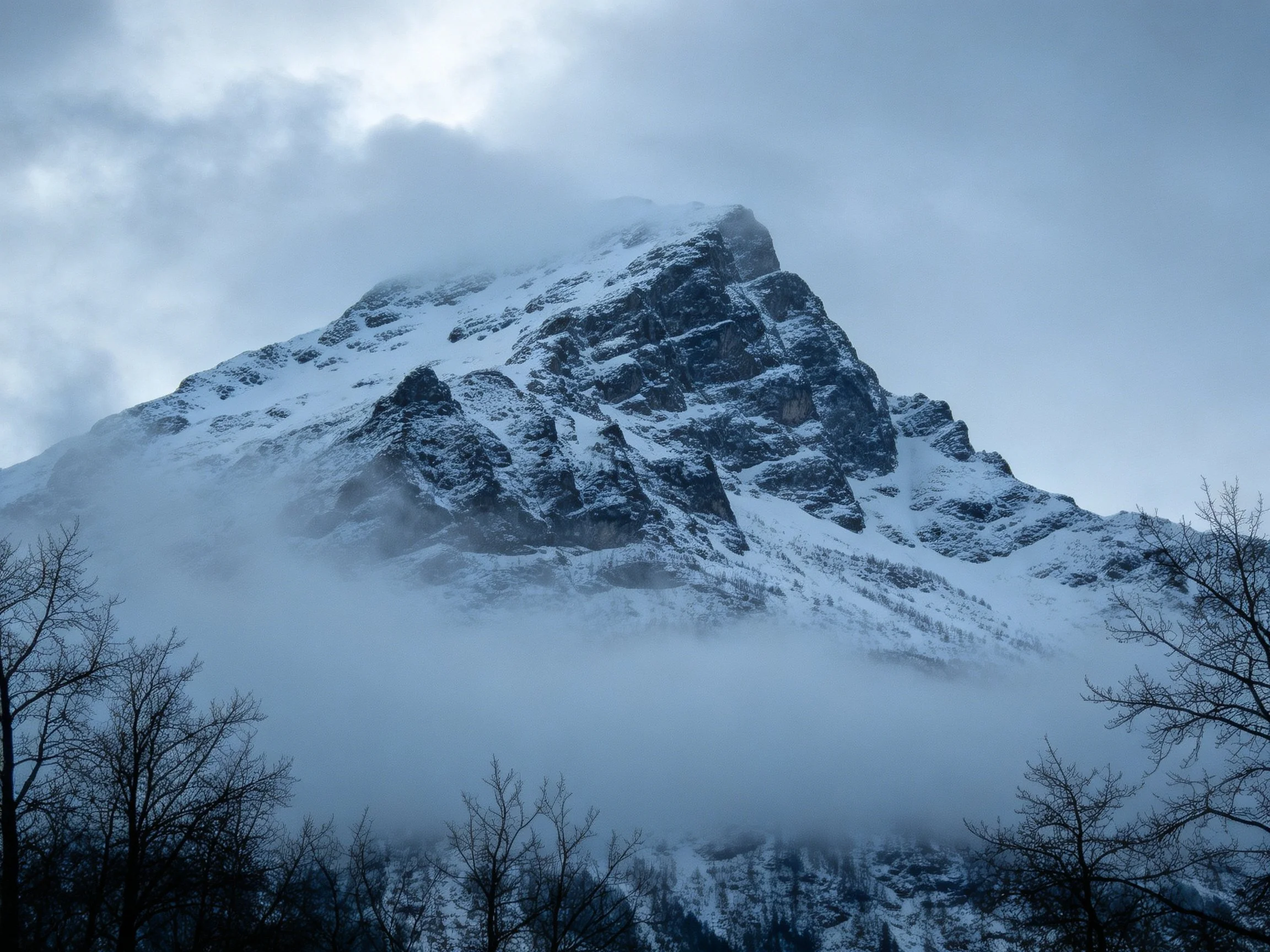 Snow-Capped Mountain Peak Shrouded in Clouds and Mist