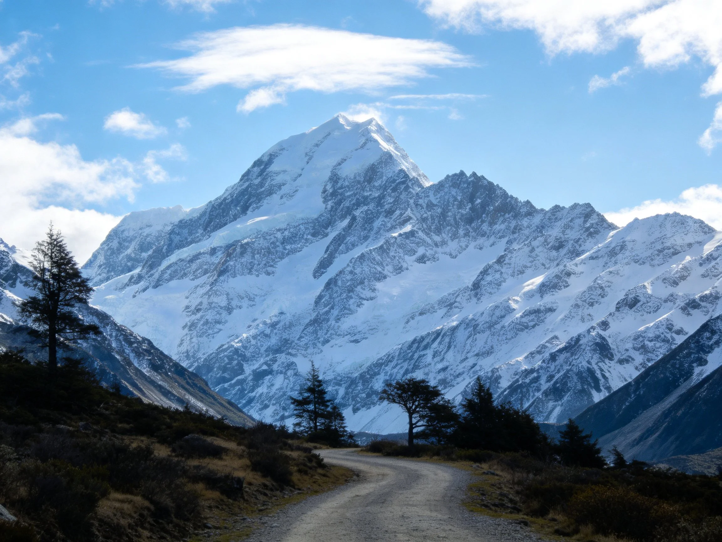 Snow - Capped Mountain Peak with Gravel Road and Clear Blue Sky