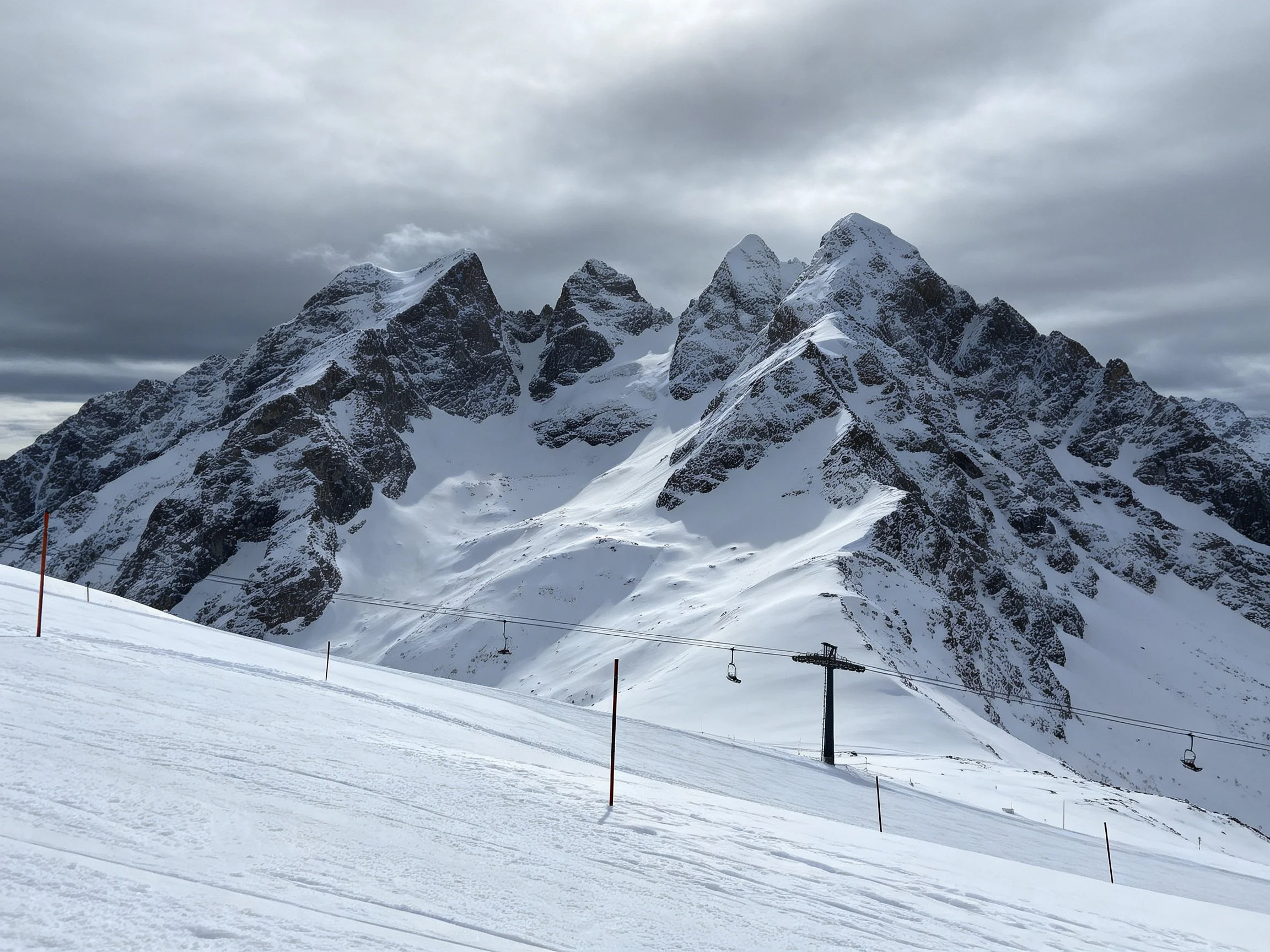 Snow-Capped Mountain Peaks with Ski Lift Infrastructure Under Cloudy Atmosphere