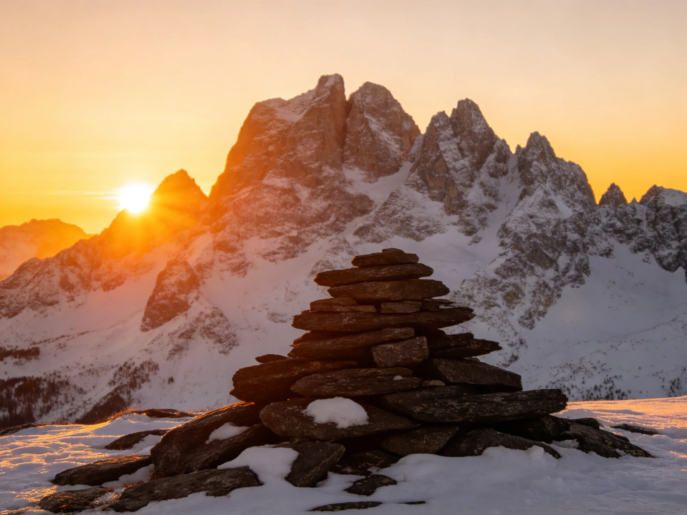 Snow-Capped Mountain Peaks with Stone Cairn at Sunset