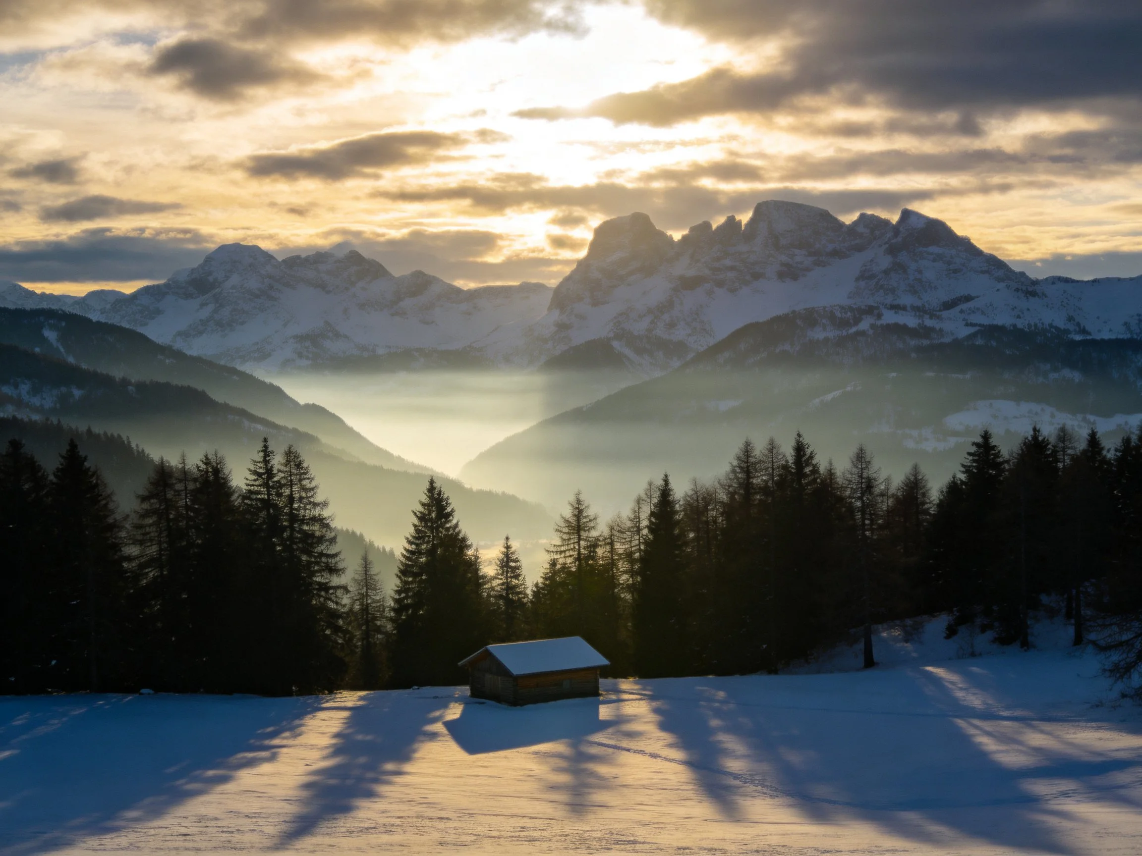Snow-Covered Mountain Peaks with Cabin and Pine Forest Under Golden Sunset