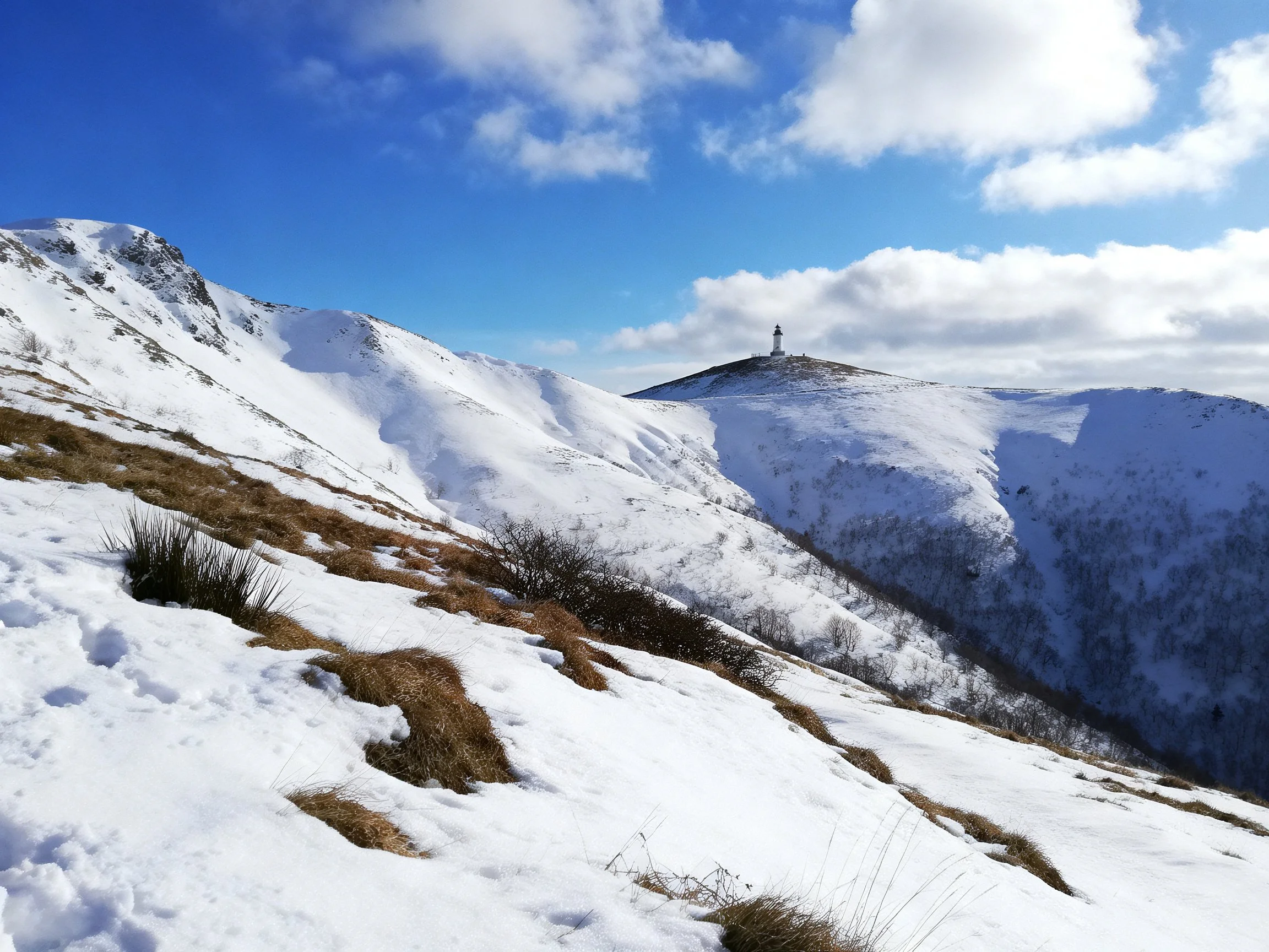 Snow-Covered Mountain Slopes with Brown Vegetation and Distant Tower