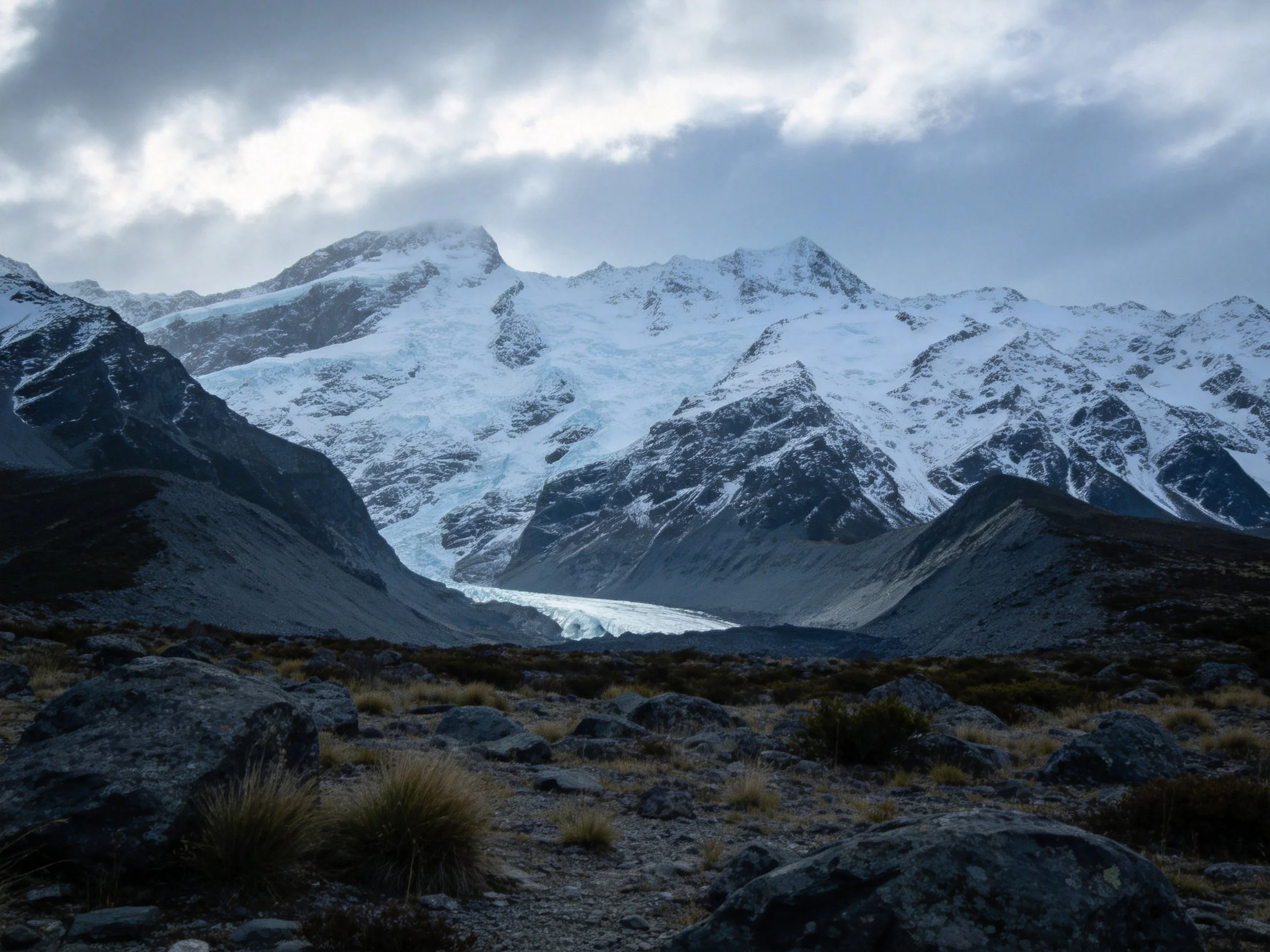 Snow-Covered Peaks with Glaciers and Rocky Terrain Under Cloudy Skies