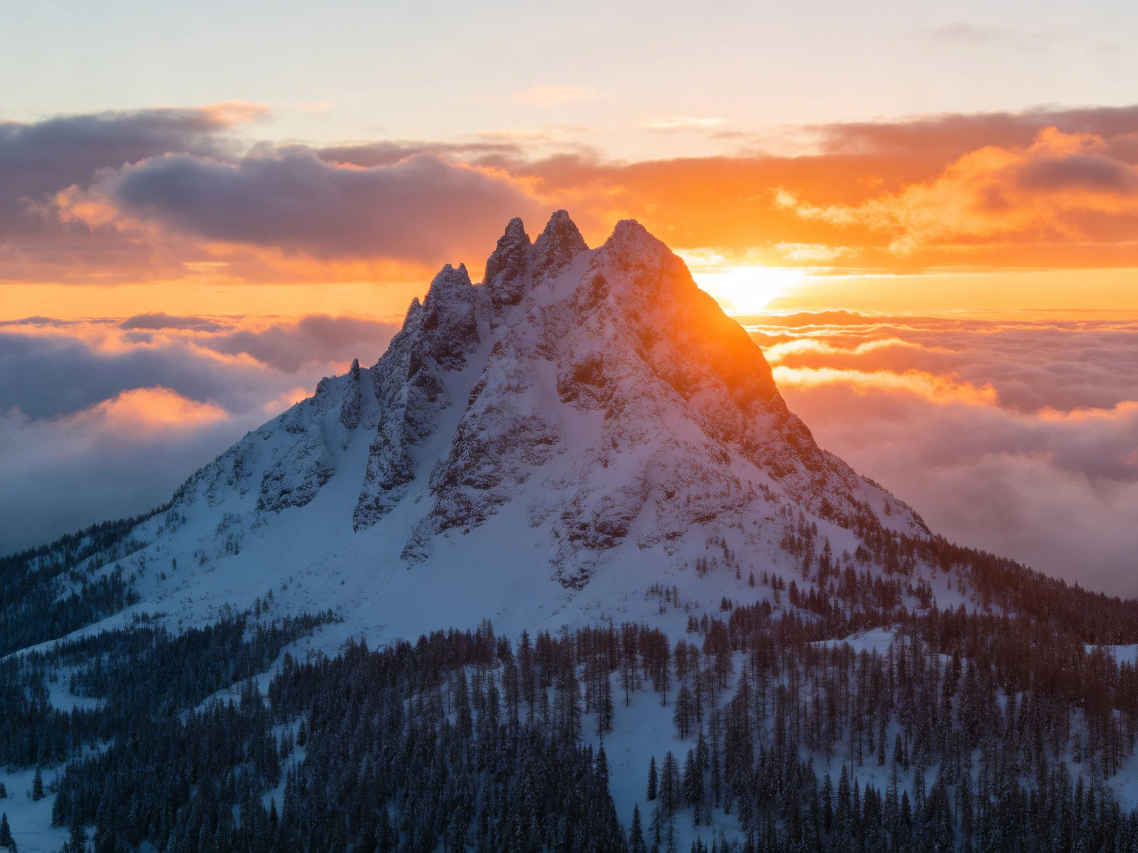 Snow-capped mountain peak at golden sunset with cloud cover