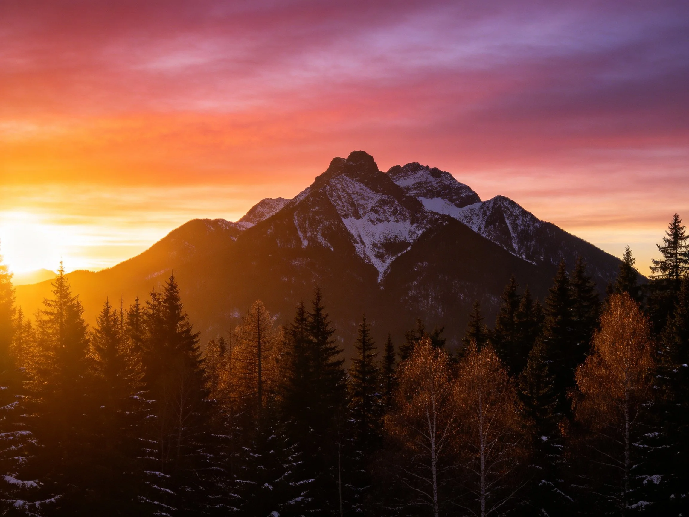Snow-capped mountain peak at vibrant sunset over forested valley