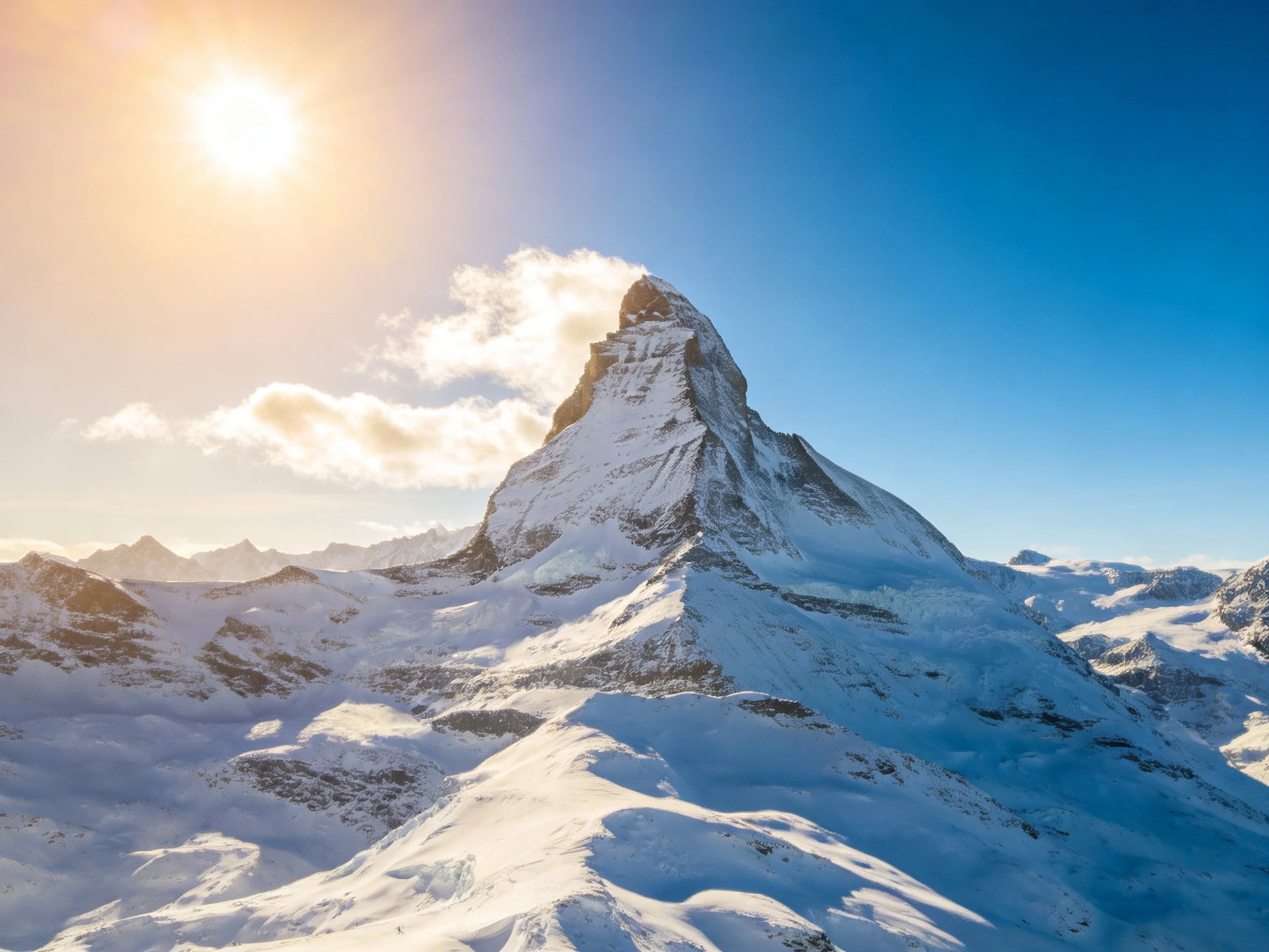 Snow-capped mountain peak bathed in golden sunlight with clear blue sky
