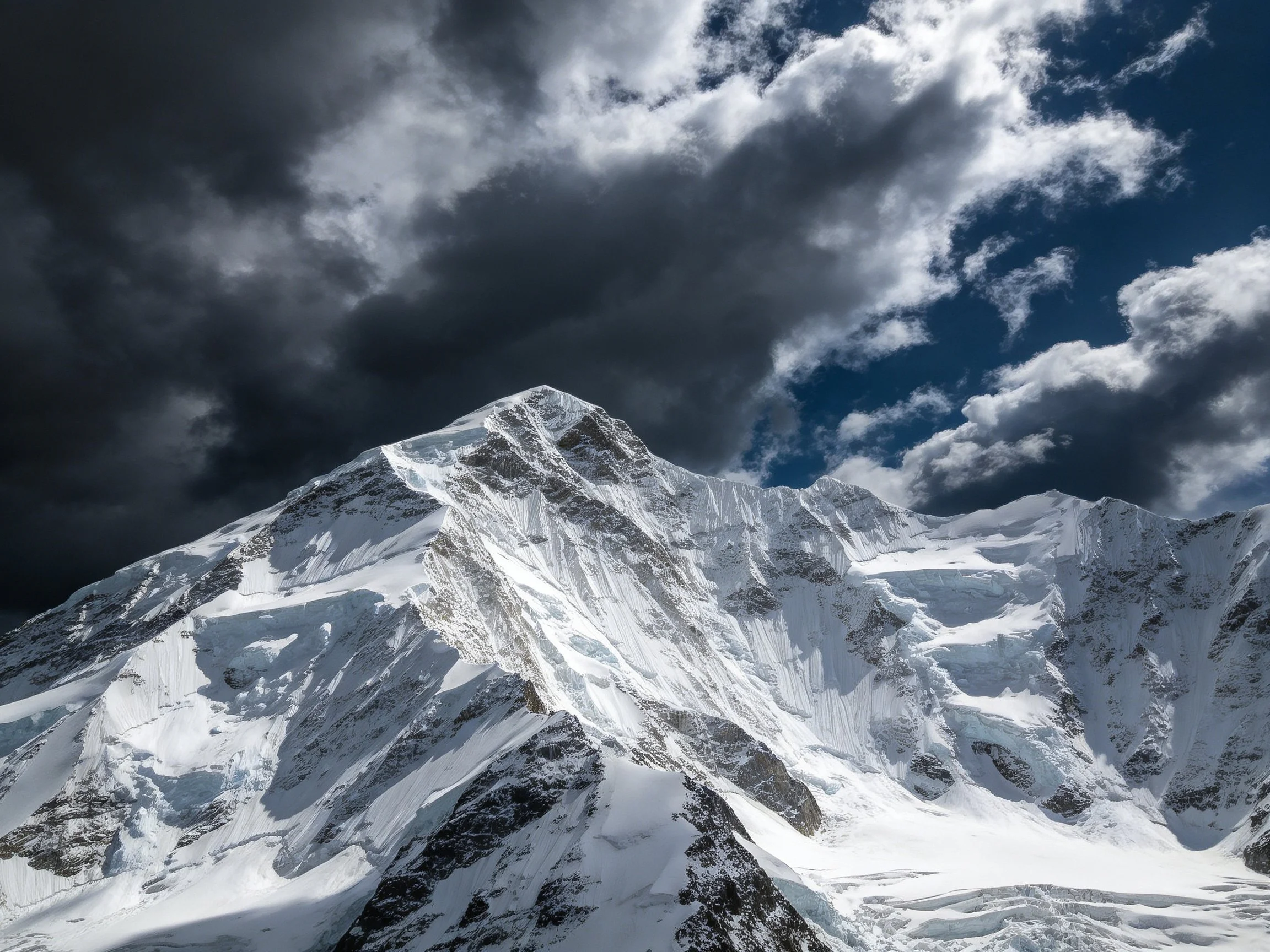 Snow-capped mountain peak beneath dramatic dark and white clouds