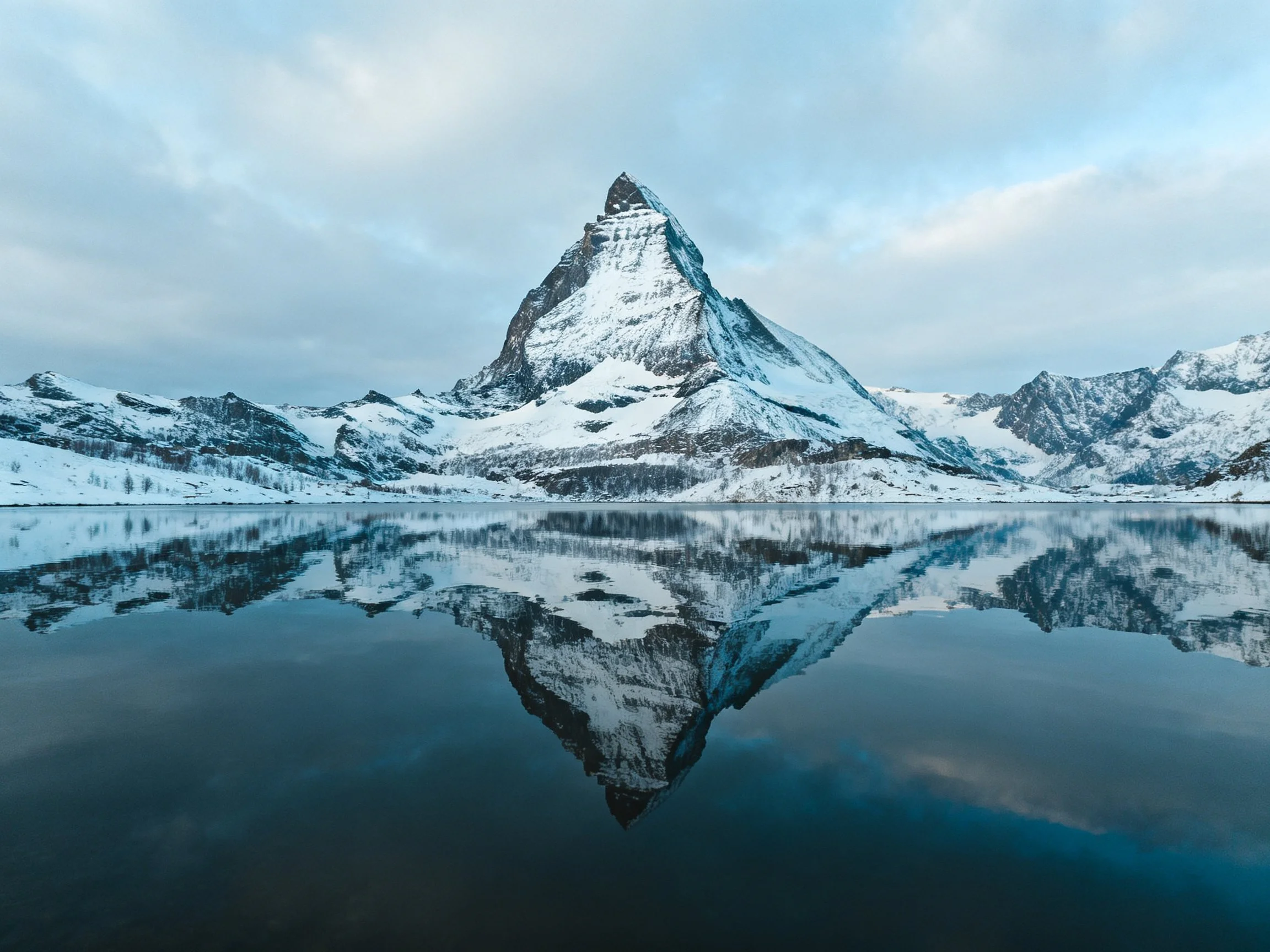Snow - capped mountain peak reflected in calm, blue - hued lake waters