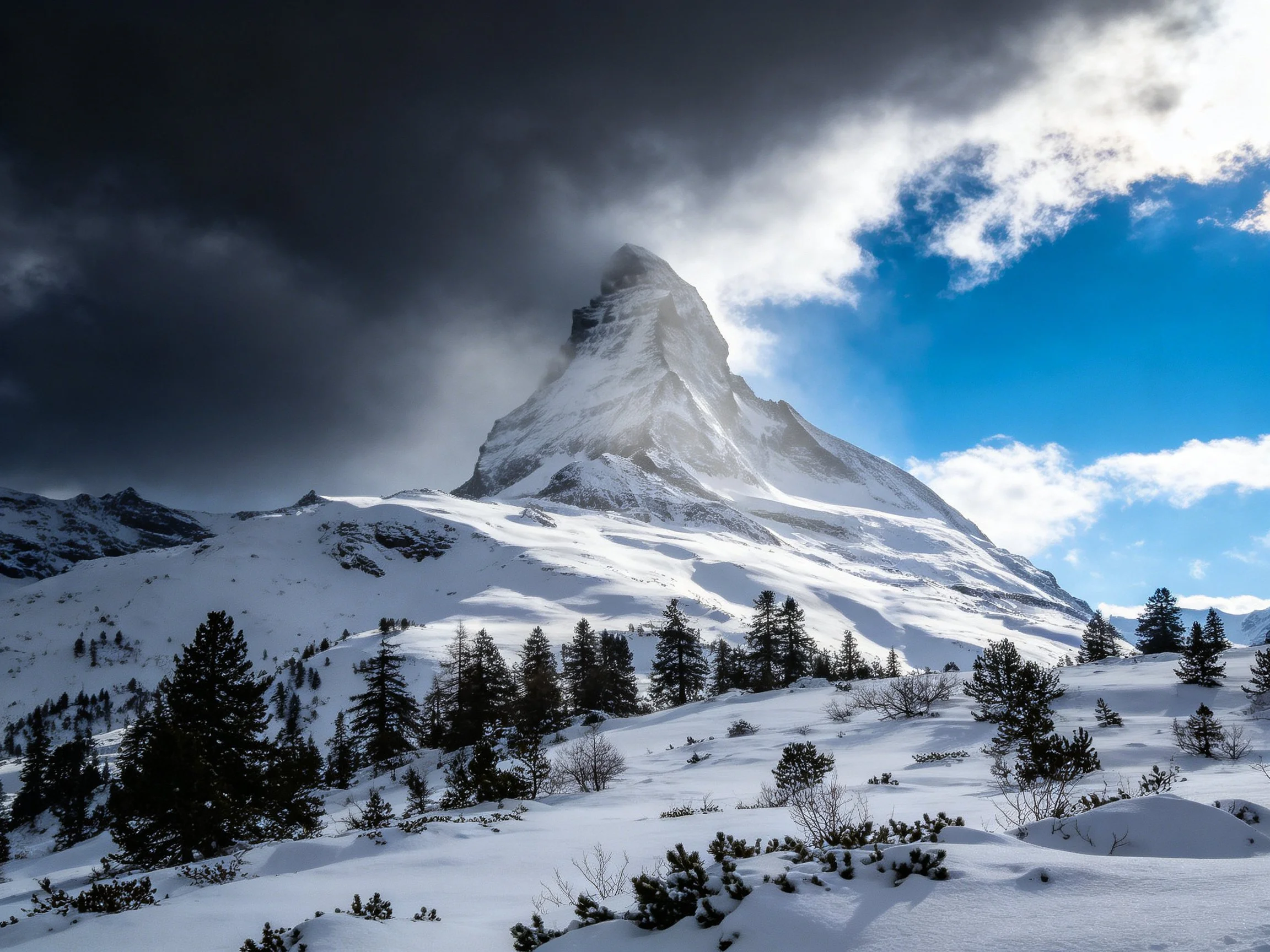Snow - capped mountain peak with contrasting stormy and sunny skies