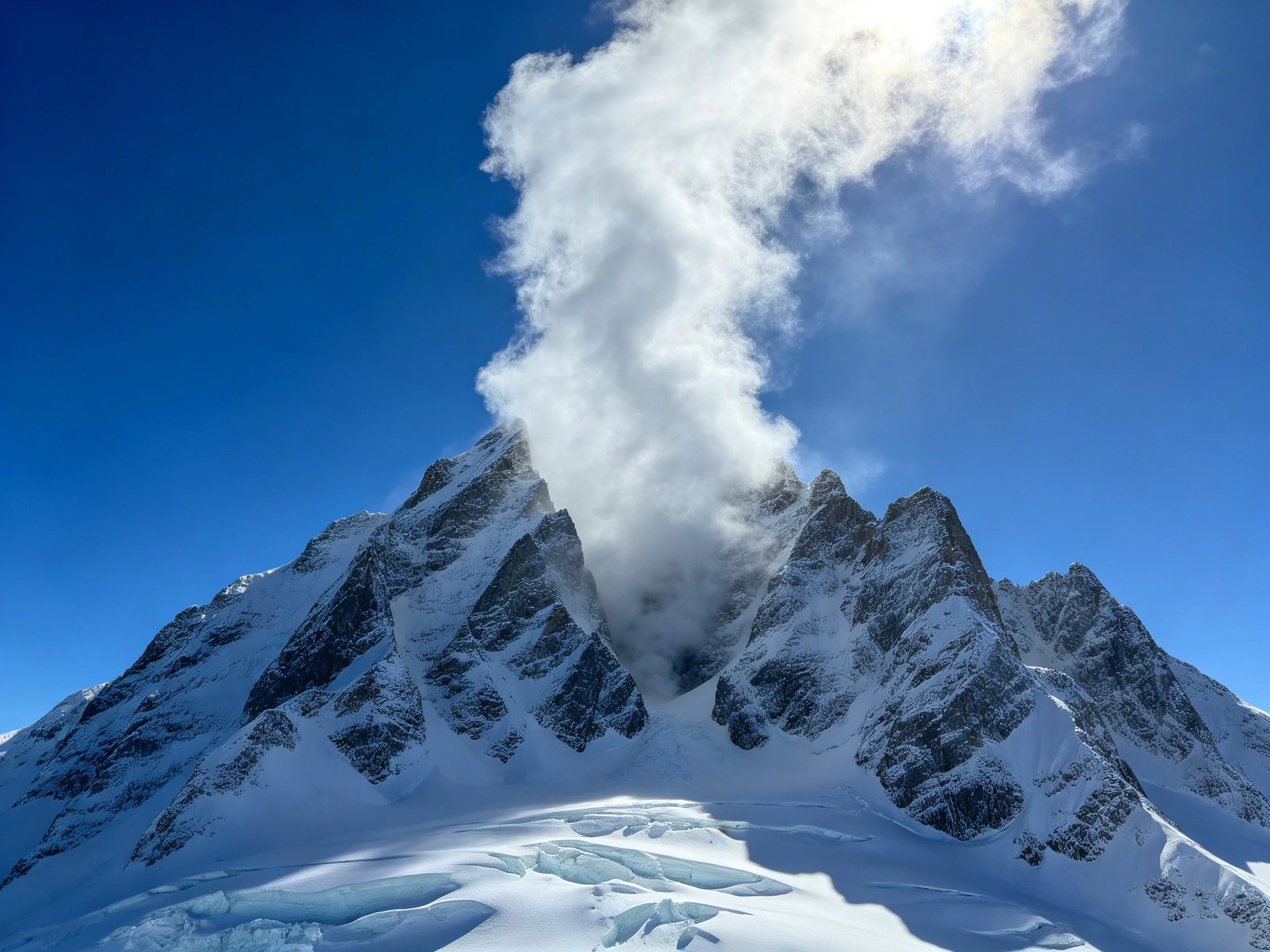 Snow - capped mountain peak with misty summit against bright blue sky