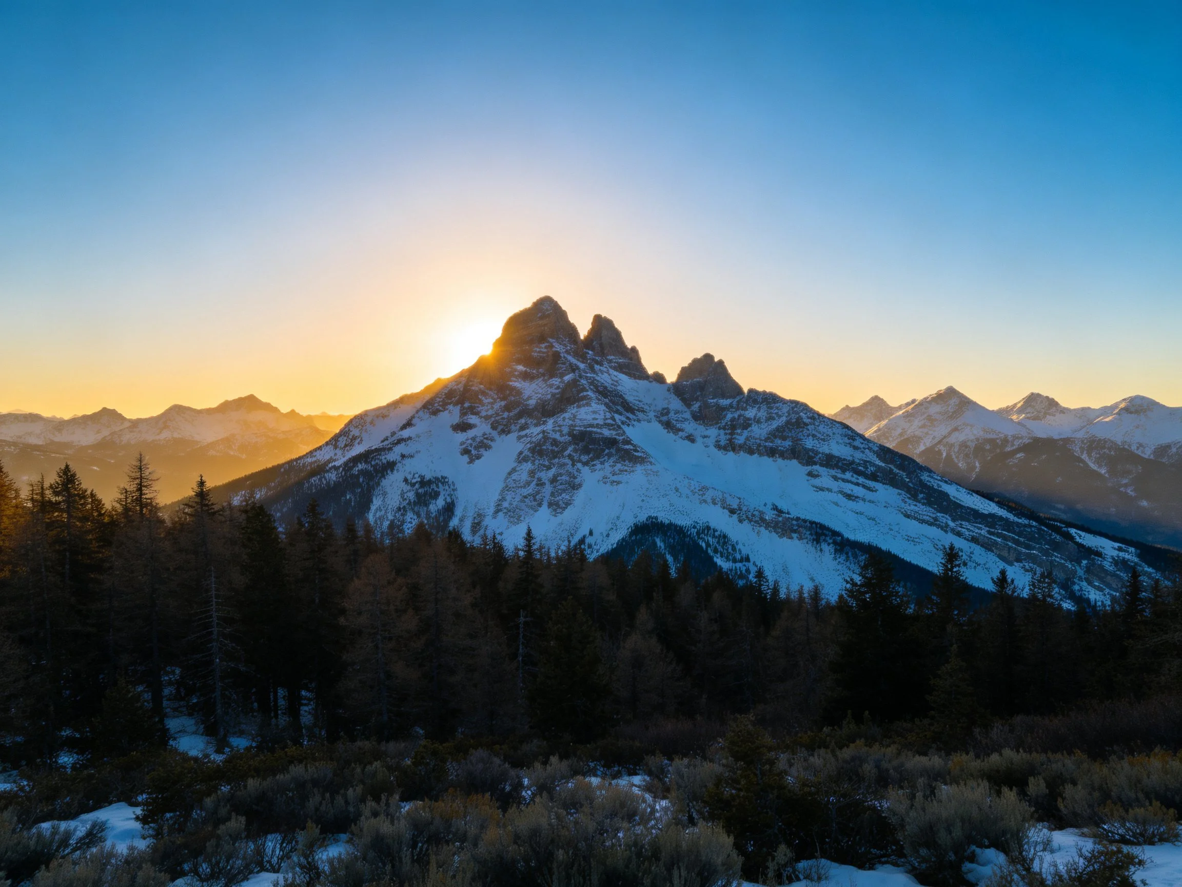 Snow - capped mountain peaks at sunset with forested foreground
