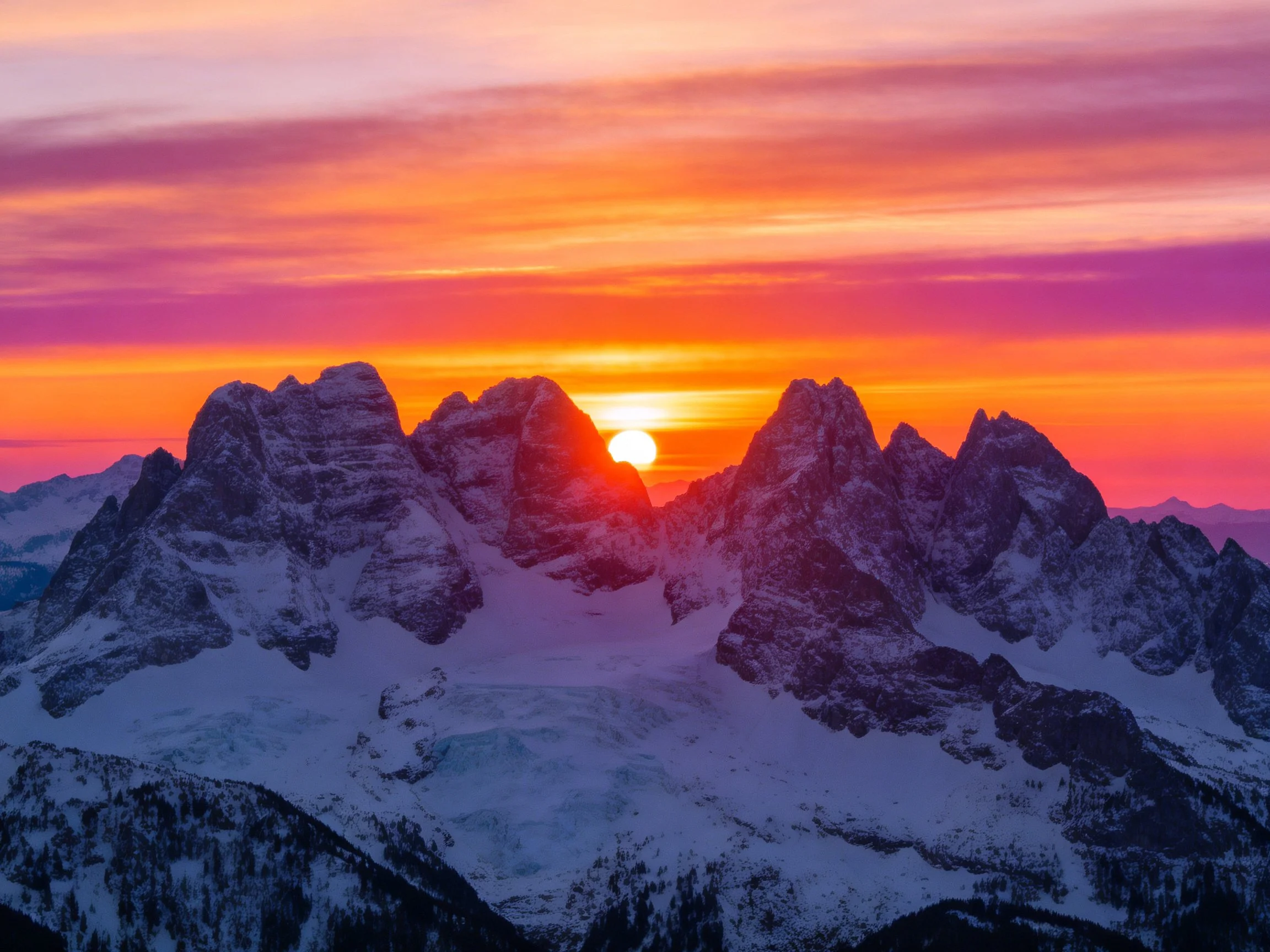 Snow-capped mountain peaks at vibrant sunset with orange-pink sky